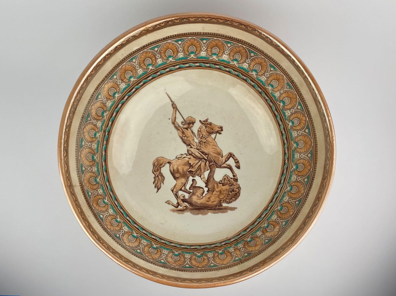 Antique European Ceramic Bowl: Antique footed bowl featuring a central motif of a warrior slaying a lion. Bowl has brown tones and bordered with neoclassical-inspired patterns. Item has stamps on the underside as pictured. Please s