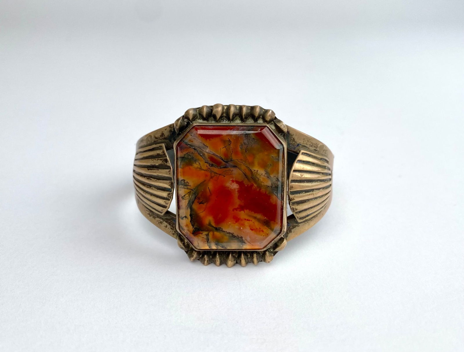 Cuff Bracelet with Rectangular Dendritic Agate Stone: A cuff bracelet featuring a bezel-set rectangular red-orange agate stone with intricate natural inclusions. The band shows fluted details on the sides and openwork design toward the edges, with patina