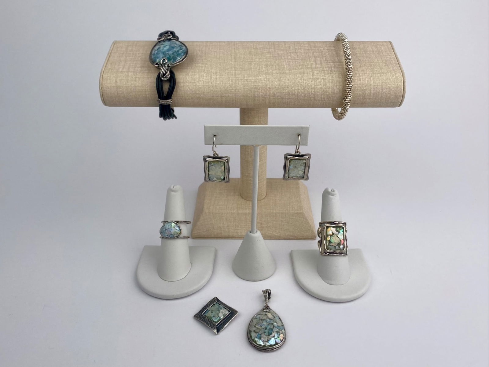 Sterling Silver Roman Glass Jewelry Set: Coordinated group of Israeli jewelry crafted in sterling silver and set with Roman glass. The set includes a pair of drop earrings, two pendants, two rings, and two bracelets. The Roman glass exhibits