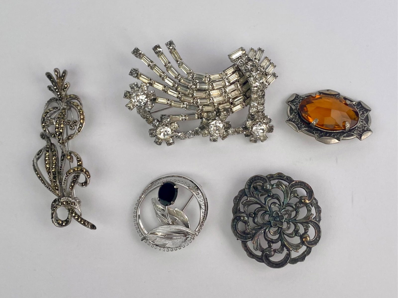 Group of Five Vintage Silver and Rhinestone Brooches: Group of five vintage brooches in silver-tone and sterling silver, featuring a mix of rhinestone, marcasite, and cabochon-set designs. Set includes a signed Weiss rhinestone spray brooch with clear ba