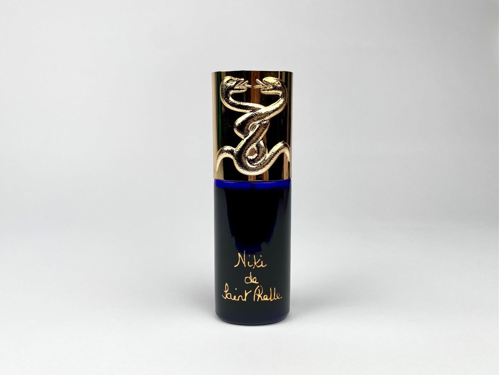 Vintage Niki de Saint Phalle Eau de Toilette with Snake Motif Cap: Niki de Saint Phalle Eau de Toilette spray bottle in a 2 fluid ounce (59 ml) size. The glass body is deep blue with “Niki de Saint Phalle” in gold lettering. The cap, designed with intertwined