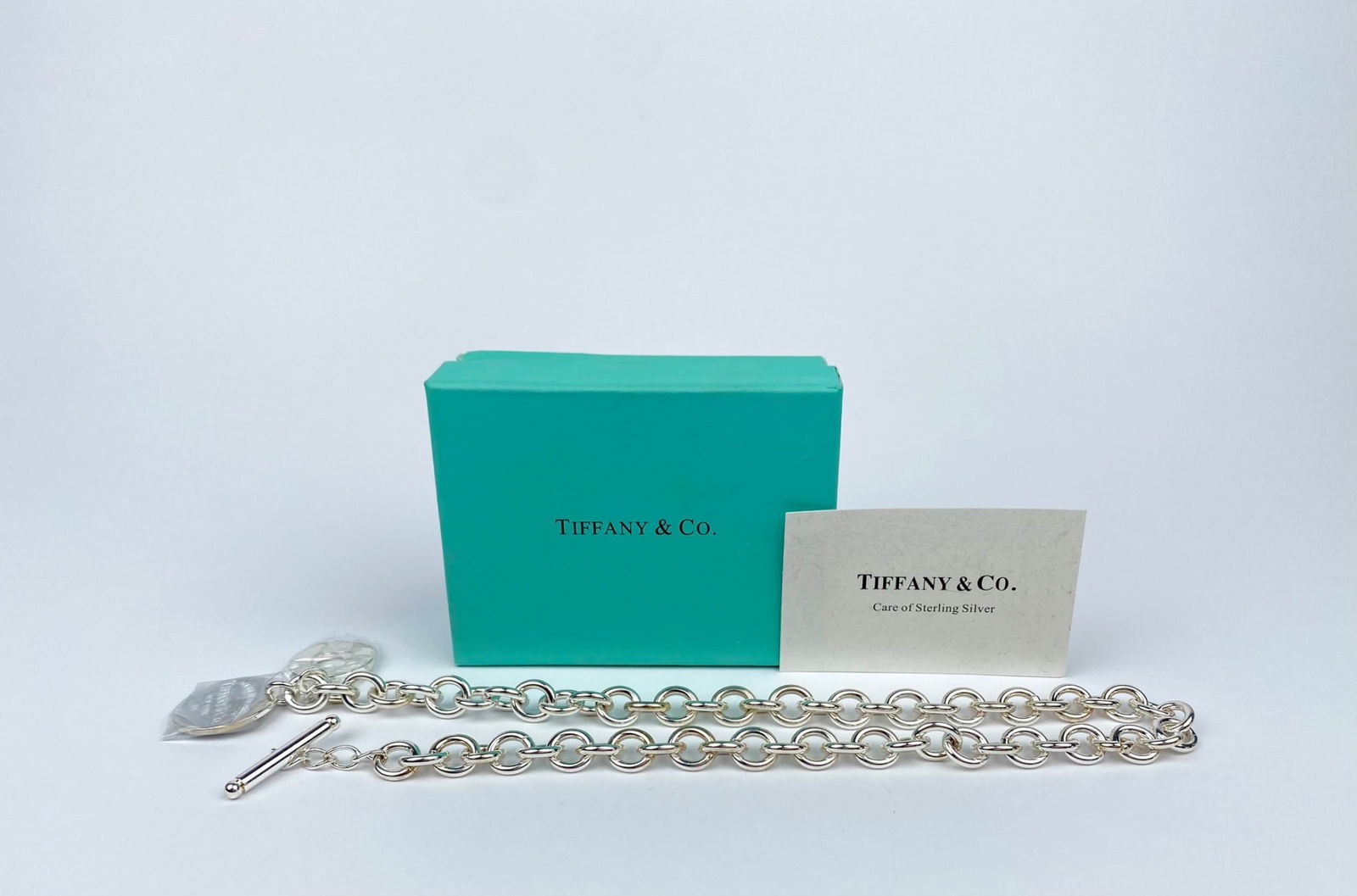 Tiffany & Co. Sterling Silver Toggle Necklace with Box & Card: Tiffany & Co. sterling silver toggle necklace, featuring a circular link chain and two charms, one engraved with ‘Please Return to Tiffany & Co.’ and another circular charm. Comes with the signatu