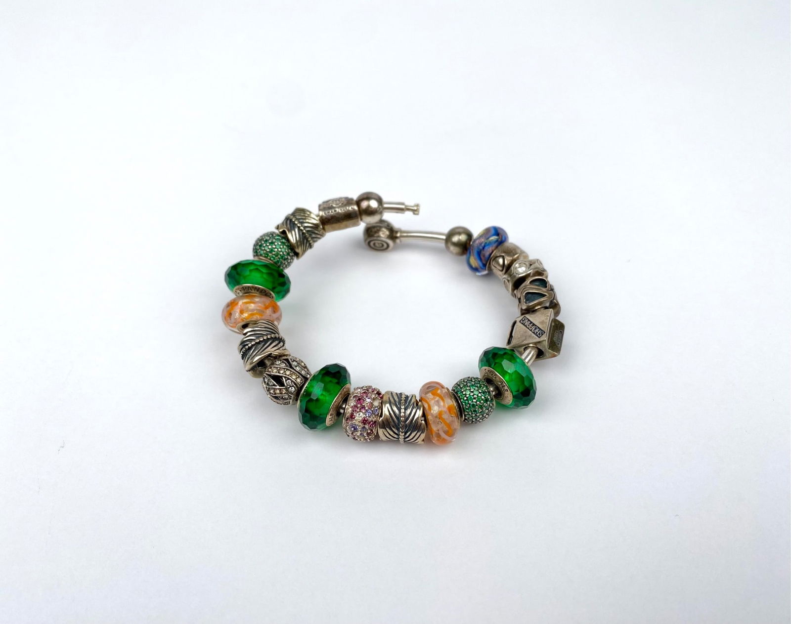 Chamilia Sterling Silver Charm Bracelet with Sterling Pandora Beads: Chamilia sterling silver charm bracelet featuring various beads in shades of green, orange, and blue, as well as intricate designs and decorative charms. The bracelet is adorned with Pandora beads tha