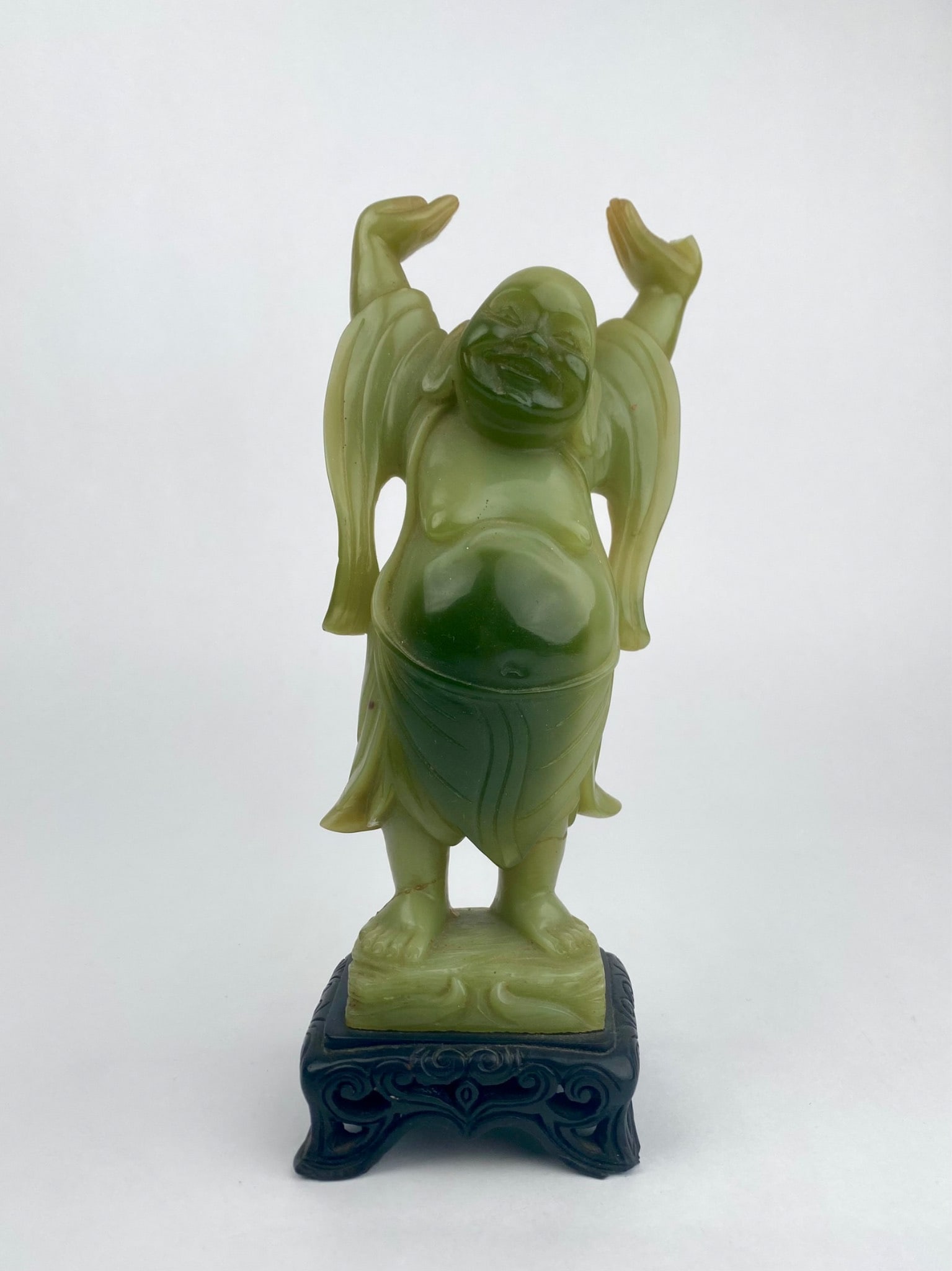 Carved Green Hardstone Laughing Buddha Figure on Stand: Carved green hardstone figure depicting a standing Laughing Buddha with raised arms, mounted on a decorative fitted stand. The figure is executed in a translucent stone with darker natural inclusions.
