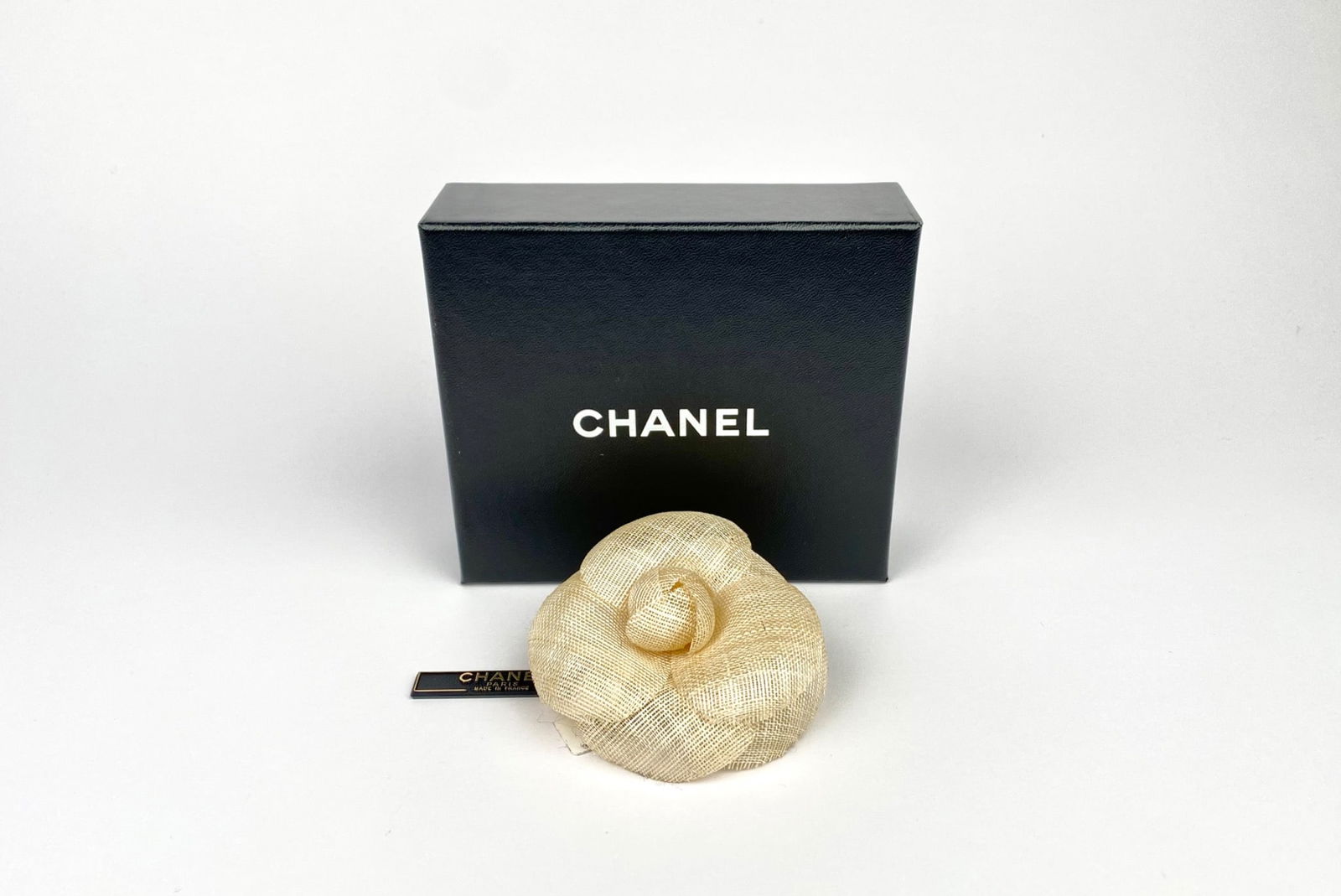 Chanel Beige Camellia Flower Brooch with Original Box: Chanel camellia flower brooch crafted from sheer, lightweight woven fabric in an ivory color. The reverse is fitted with a gold-tone pin-back closure and retains the original oval Chanel plaque. The b