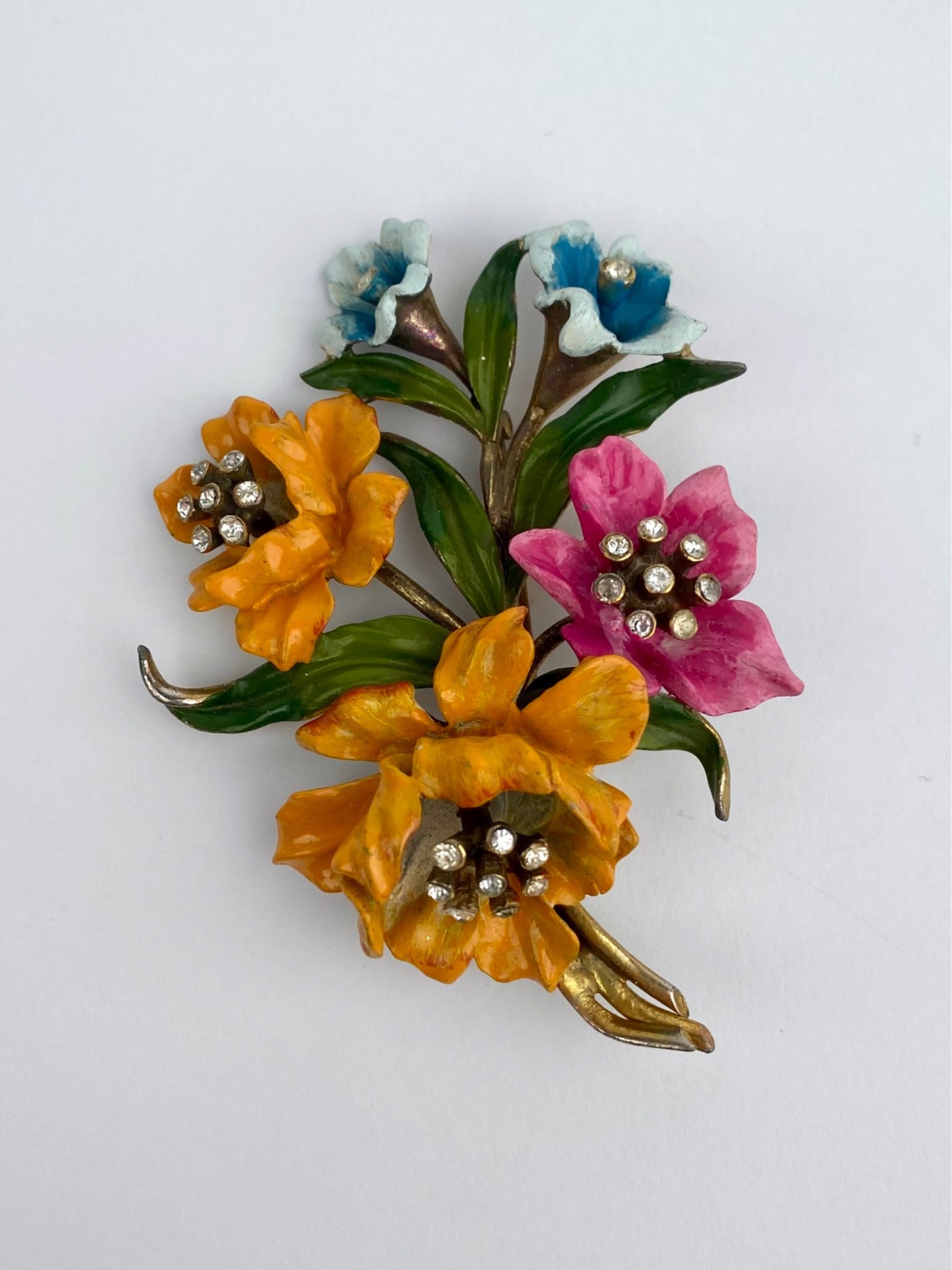 Vintage Enamel Floral Rhinestone Bouquet Brooch: Vintage floral bouquet brooch featuring hand-painted enamel flowers in shades of orange, pink, blue and green with clear rhinestones centers. The dimensional design is executed in gold-tone metal with