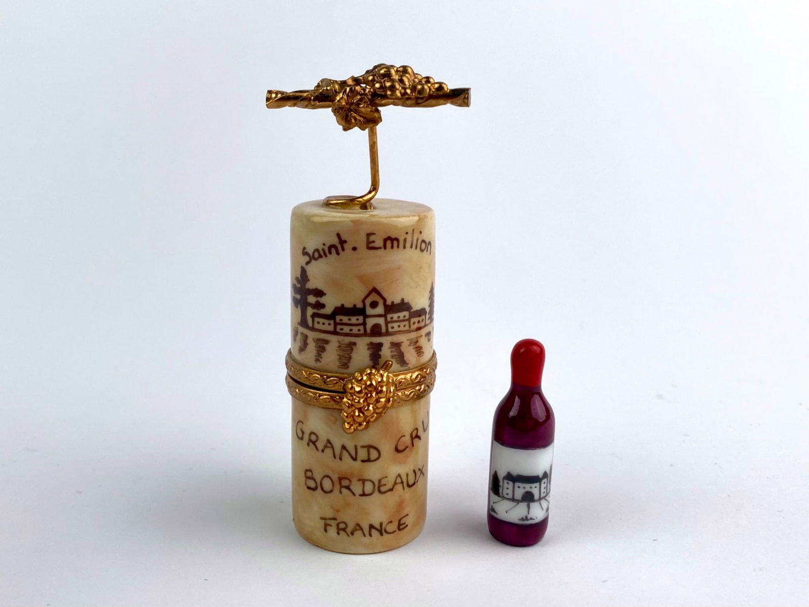 French Limoges Porcelain Wine Cork Trinket Box: Hand-painted French Limoges porcelain trinket box designed in the form of a wine cork, decorated with Saint-Emilion village imagery and inscribed “Grand Cru Bordeaux France.” The cylindrical b