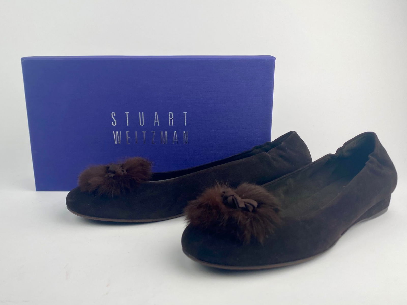 Stuart Weitzman 'Furball' Brown Suede Flats with Fur Trim, Size 9.5: Pair of women's Stuart Weitzman "Furball" flats crafted in brown suede, featuring a rounded toe accented with a fur pom-pom and suede bow detail. The shoes have low stacked heels, leather interiors, a