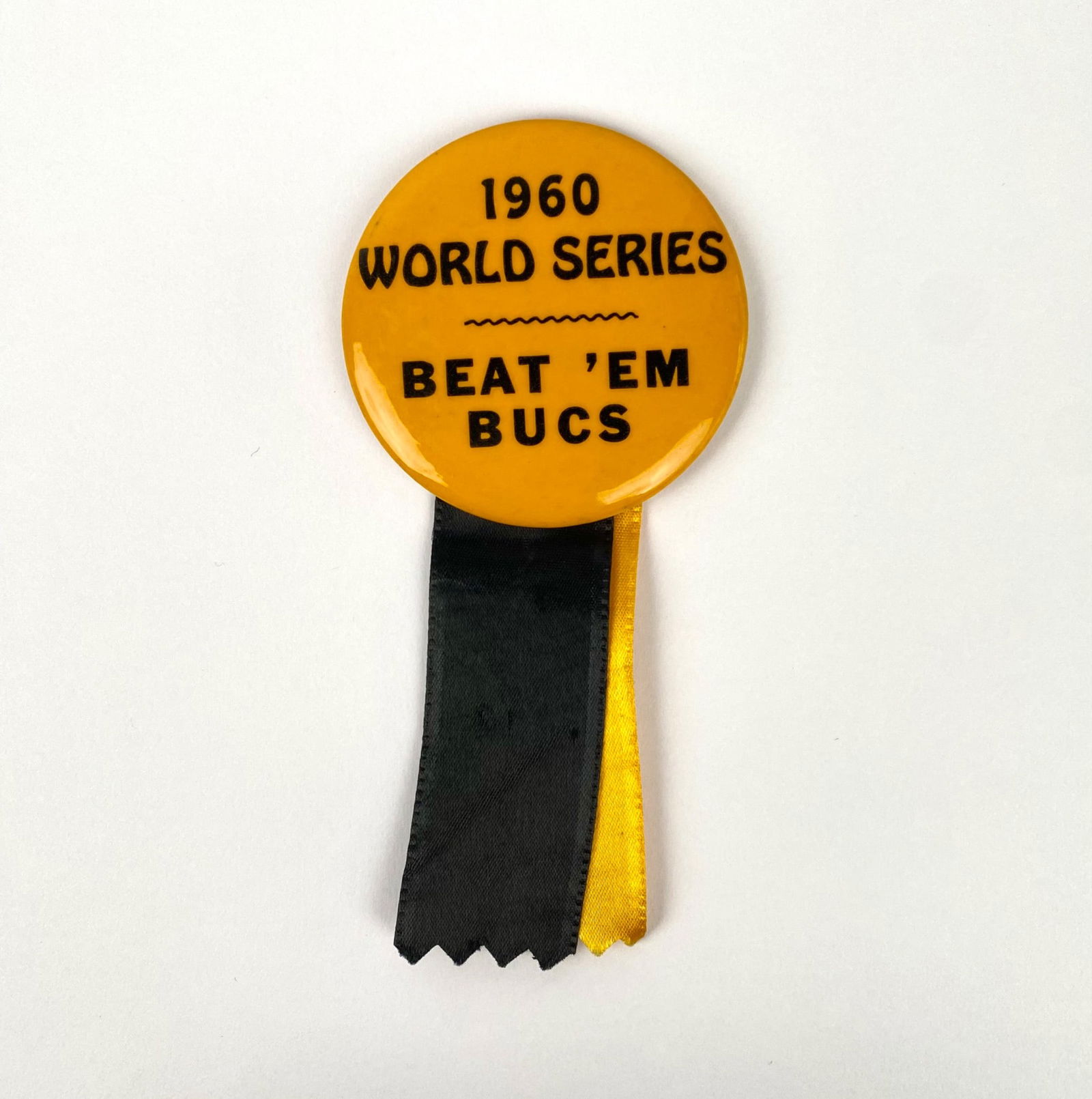 1960 World Series ‘Beat ‘Em Bucs’ Button with Ribbons: A vintage button from the 1960 World Series featuring the text “1960 World Series Beat ‘Em Bucs.” The button is crafted from metal with attached gold and black ribbon accents. The pinback me