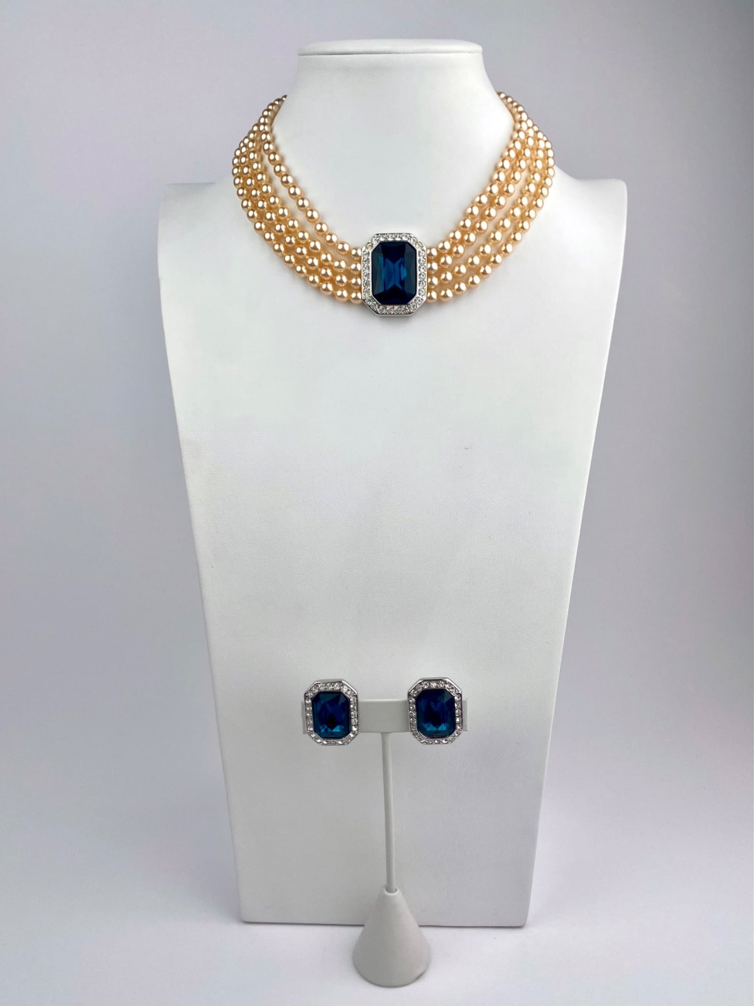 Kenneth Jay Lane Faux Pearl and Blue Rhinestone Necklace & Earrings Set: Coordinated jewelry set by Kenneth Jay Lane, consisting of a multi-strand faux pearl necklace and matching earrings. The necklace features multiple strands of ivory-toned faux pearls, centered by an o