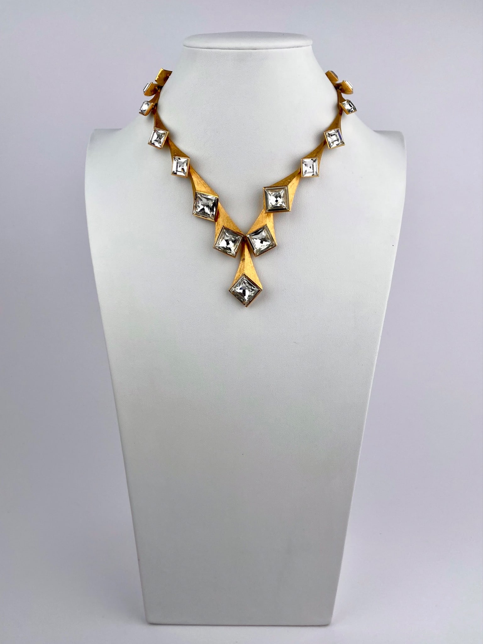 Vintage Gold-Tone Geometric Rhinestone Necklace: Vintage gold tone necklace featuring an articulated geometric design set with clear square cut rhinestones. The necklace is composed of angular, tapered panels with brushed gold-tone surfaces, each ce