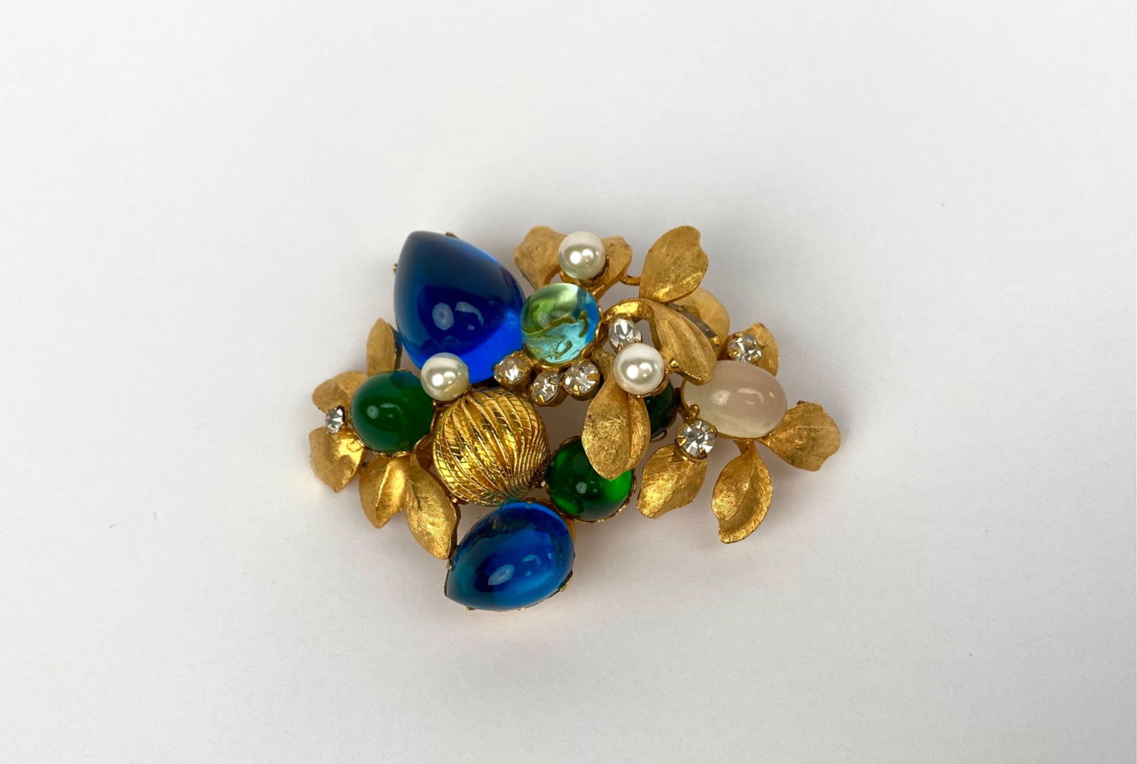 Vintage Gold-Tone Cluster Brooch with Blue & Green Cabochons: Gold-tone brooch featuring a textured leafy design, adorned with blue and green glass cabochons, faux pearls, and clear rhinestones. The centerpiece includes a gold-tone decorative element. The revers