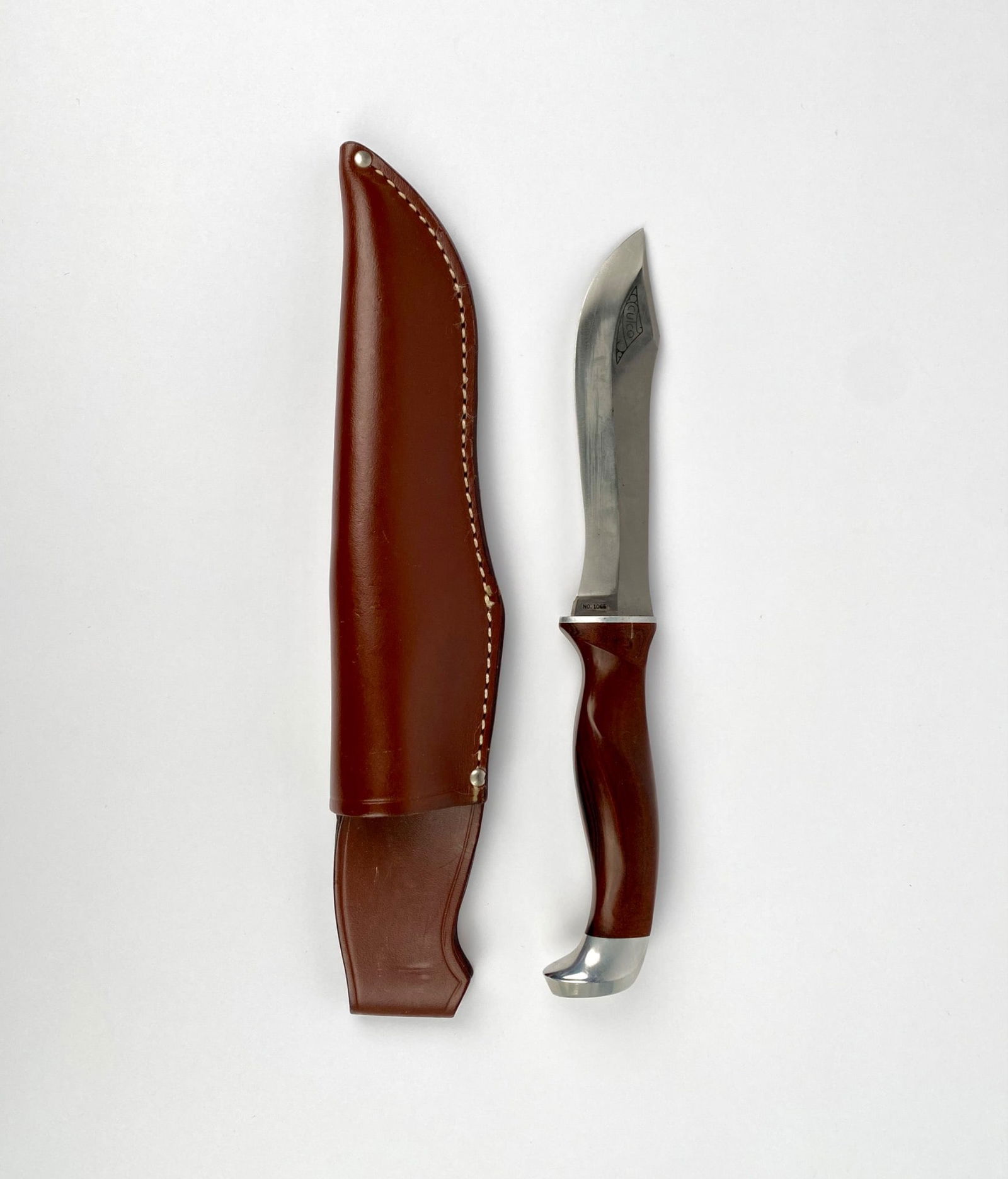 Cutco No. 1065 Hunting Knife with Leather Sheath: Cutco NO. 1065 fixed blade knife featuring a polished stainless steel blade with decorative engraving near the spine. The handle is crafted from a polished wood-like material, designed for ergonomic g