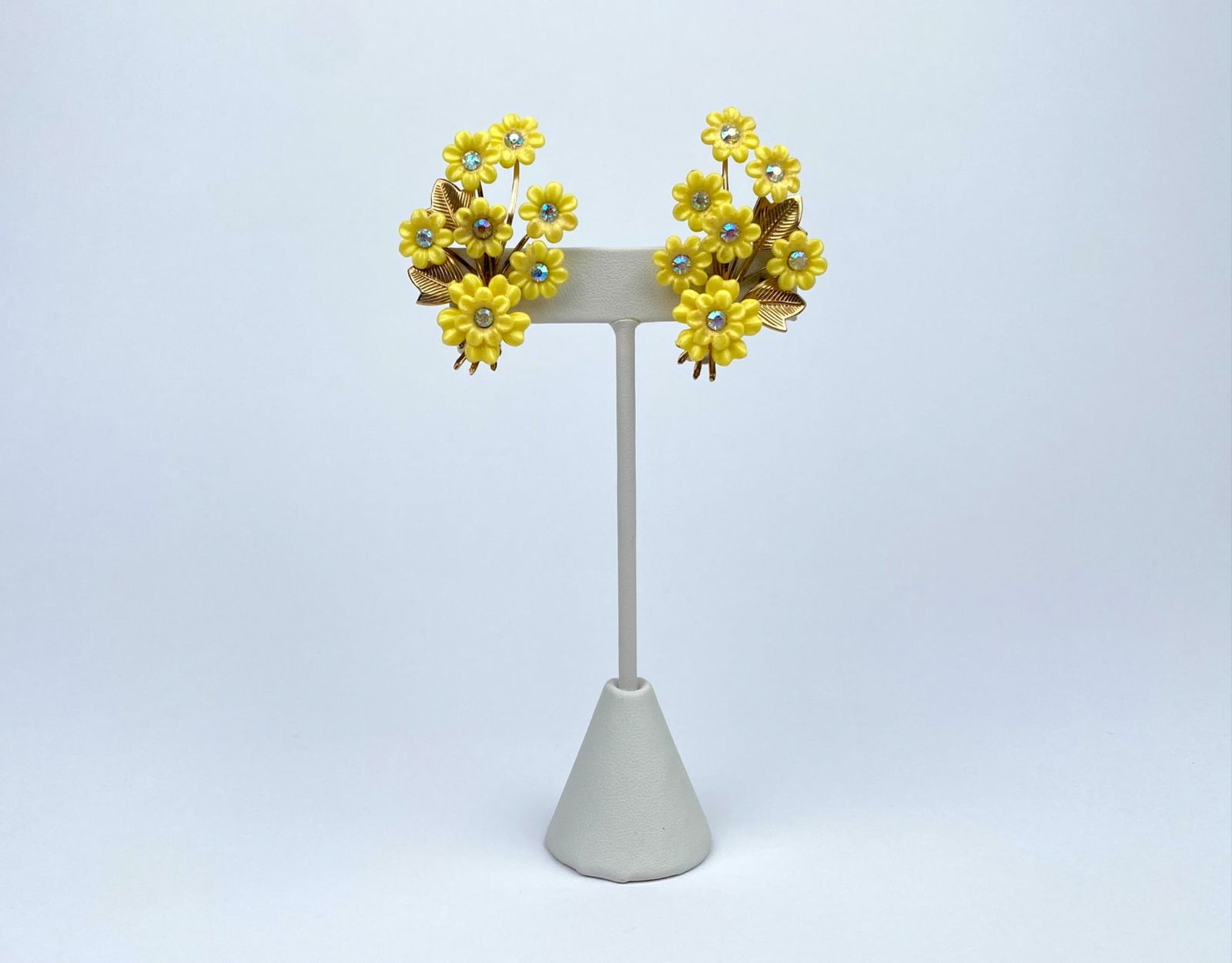 Vintage Coro Yellow Floral Clip-On Earrings with Rhinestone Accents: Vintage floral clip-on earrings featuring vibrant yellow resin flowers embellished with rhinestone centers. The earrings include gold-toned metal leaves and stems for added detail. The clips on the re