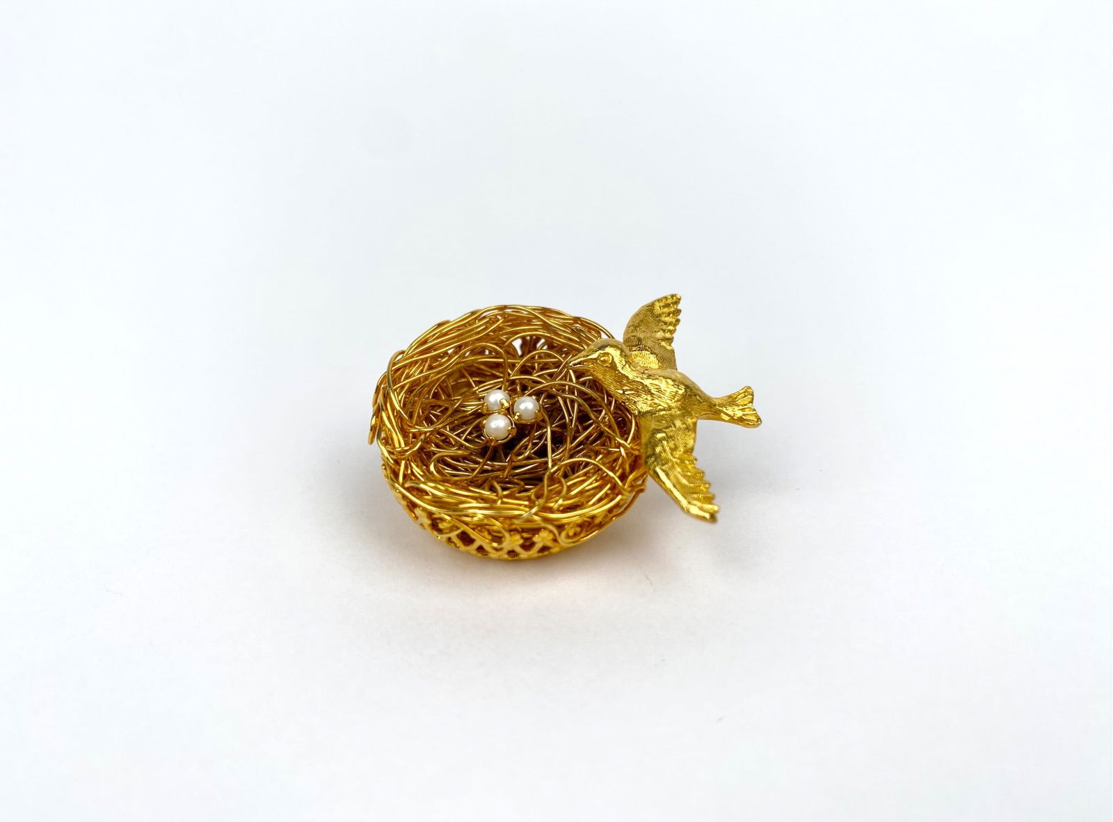 Jeanne Gold-Tone Bird & Nest Brooch with Faux Pearls: Gold-tone brooch featuring a bird perched on a delicately crafted nest containing three faux pearls. The intricate filigree design adds dimension and texture to the piece. Marked with “Kramer”