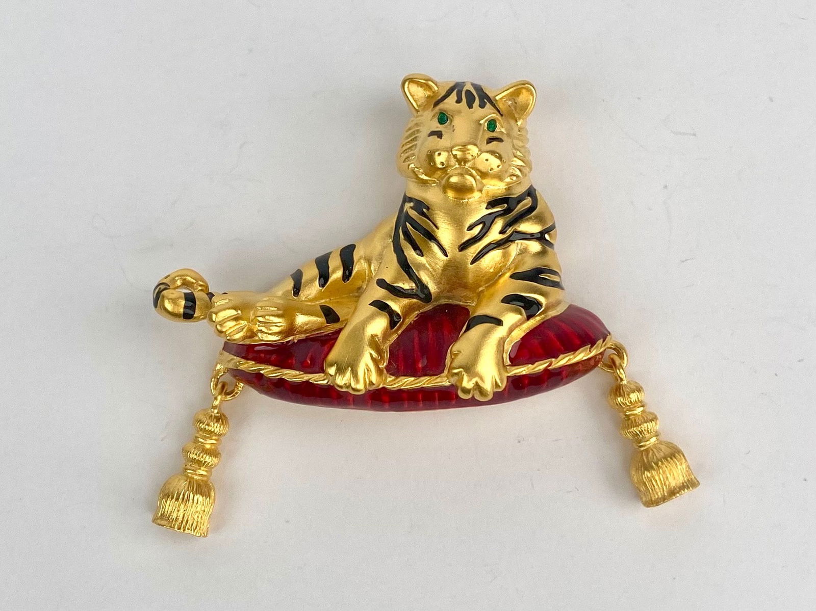 Bob Mackie Signed Tiger Brooch with Red Cushion and Tassels: Signed Bob Mackie figural gold-tone brooch depicting a reclining tiger resting on a red cushion with articulated tassel drops. The tiger features sculptural detailing with black enamel striping and gr