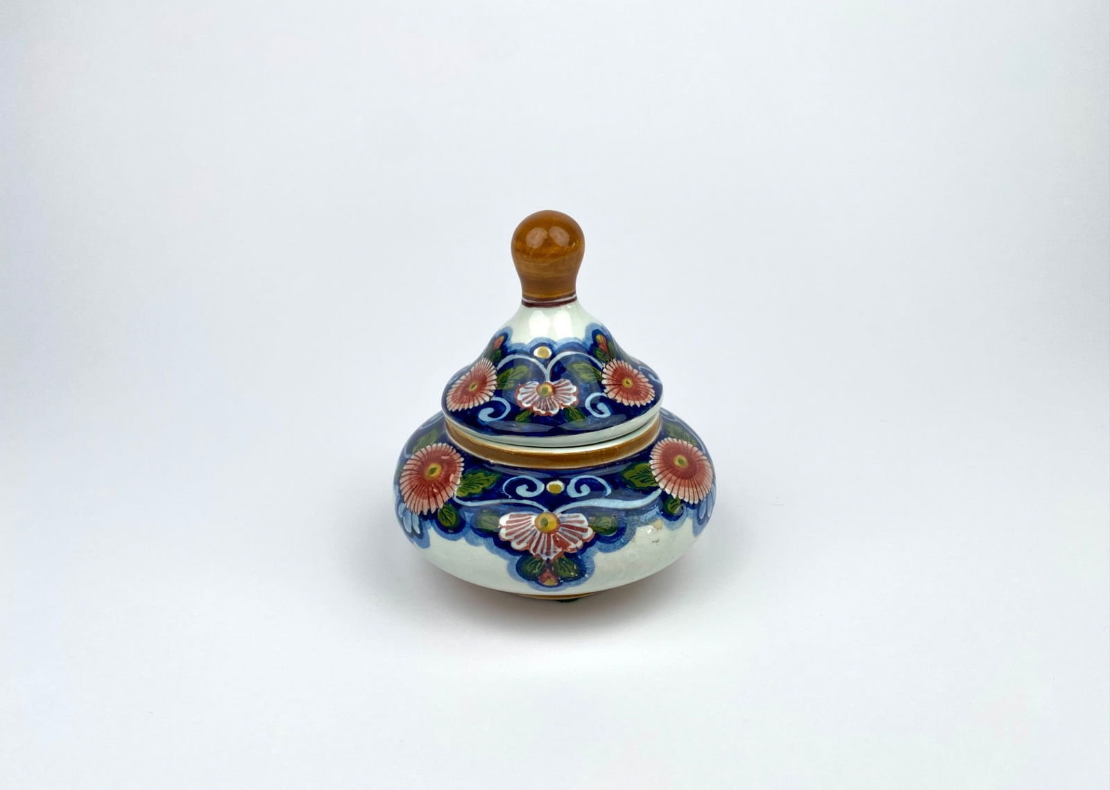 Polychrome Delft Hand-Painted Ceramic Lidded Jar, Holland: Hand-painted ceramic lidded jar, crafted by Delft, featuring vibrant floral motifs. Adorned with a wooden finial on the lid. The piece is marked “Delft 100% Handwerk Holland” on the underside,