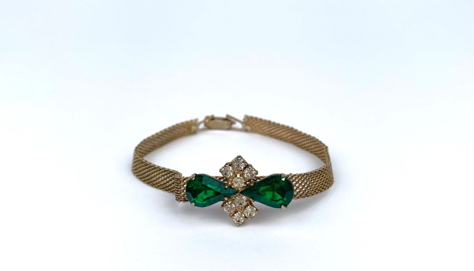 Vintage Gold-Tone Mesh Bracelet with Green & Clear Stone Accents: Gold-tone mesh bracelet featuring a central decorative element with two green, pear-shaped stones and clear rhinestones forming a bow-like motif. The bracelet is secured with a fold-over clasp. | Plea