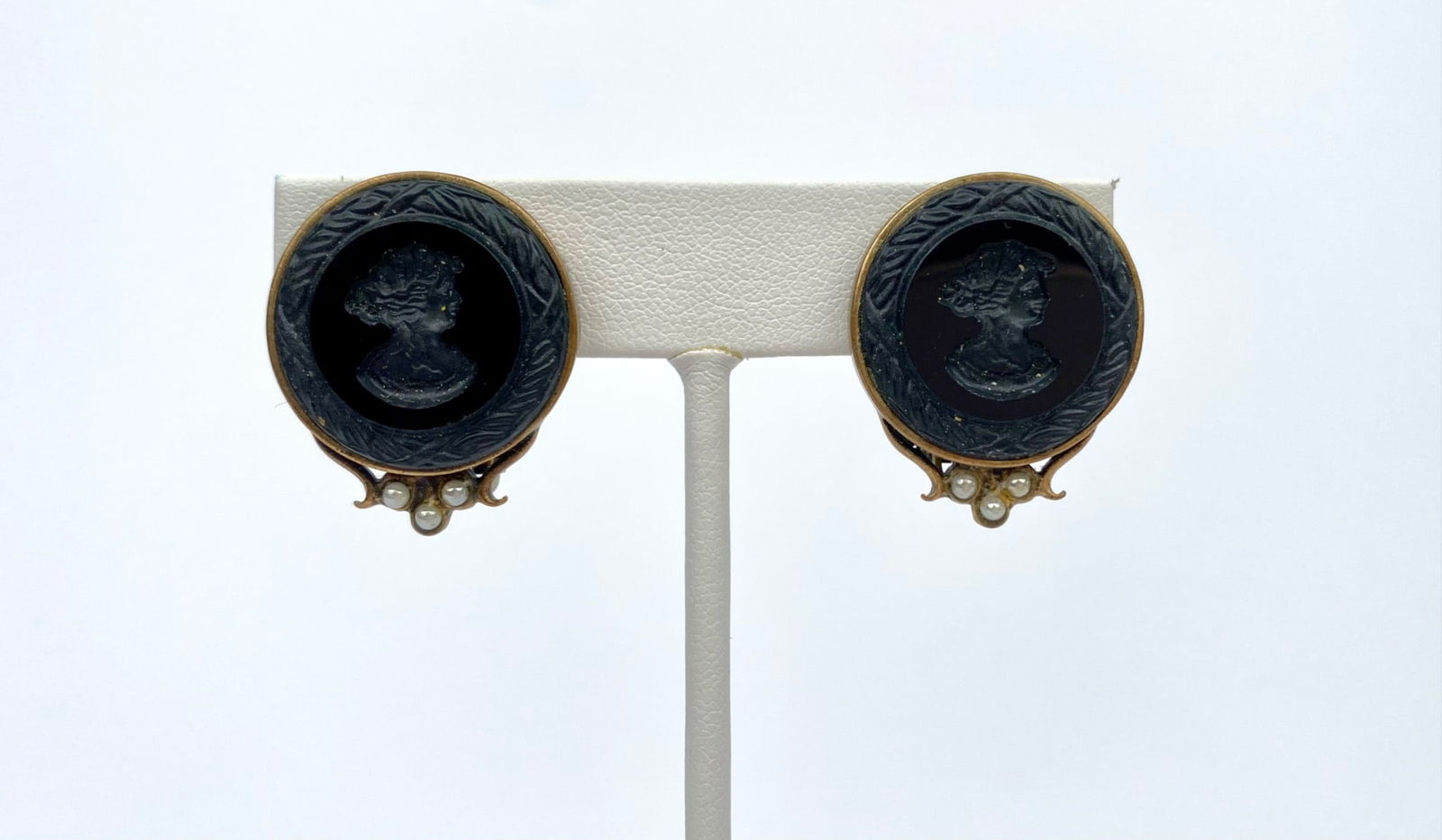 Vintage Black Cameo Clip-On Earrings with Faux Pearl Accents: Gold-tone cameo-style clip-on earrings featuring black circular settings with embossed profiles of a woman. Each earring is accented with three small faux pearls below the cameo. Backings are clip-on
