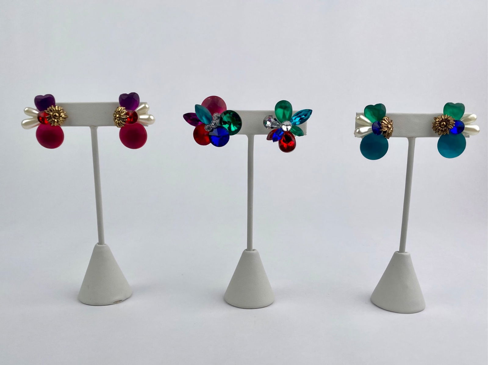 Three Pairs of Colorful Lucite Floral Clip-On Earrings: Set of three vintage clip-on earrings, each featuring bold floral-inspired designs composed of Lucite elements in jewel tones. All three pairs are clip-back style and unmarked. Set is in good conditio