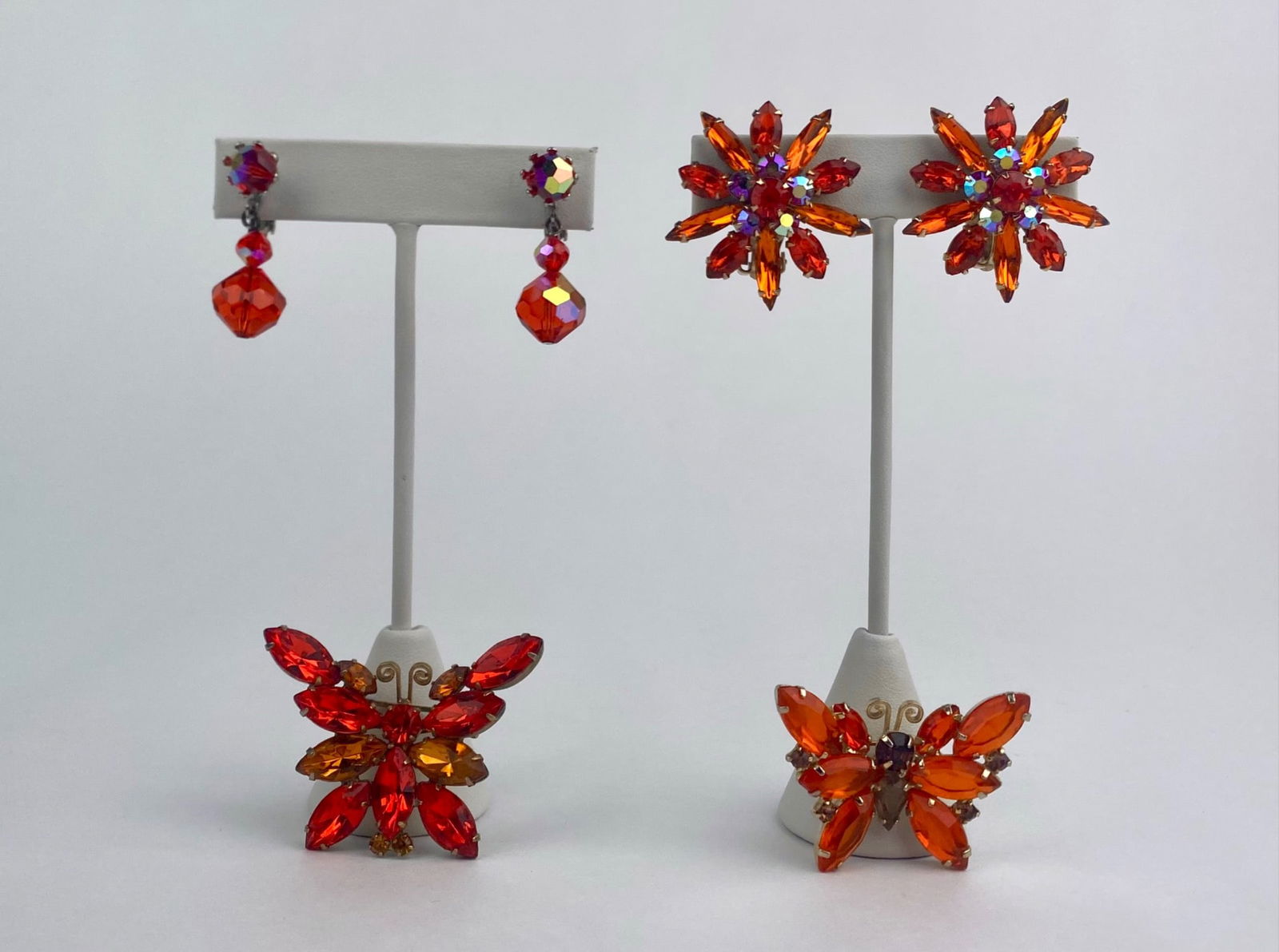 Orange Rhinestone Earrings and Butterfly Brooch Set: Vintage costume jewelry set featuring orange and amber-toned rhinestones. The group includes two pairs of clip-on earrings, one starburst floral form with marquise-cut stones and aurora borealis accen