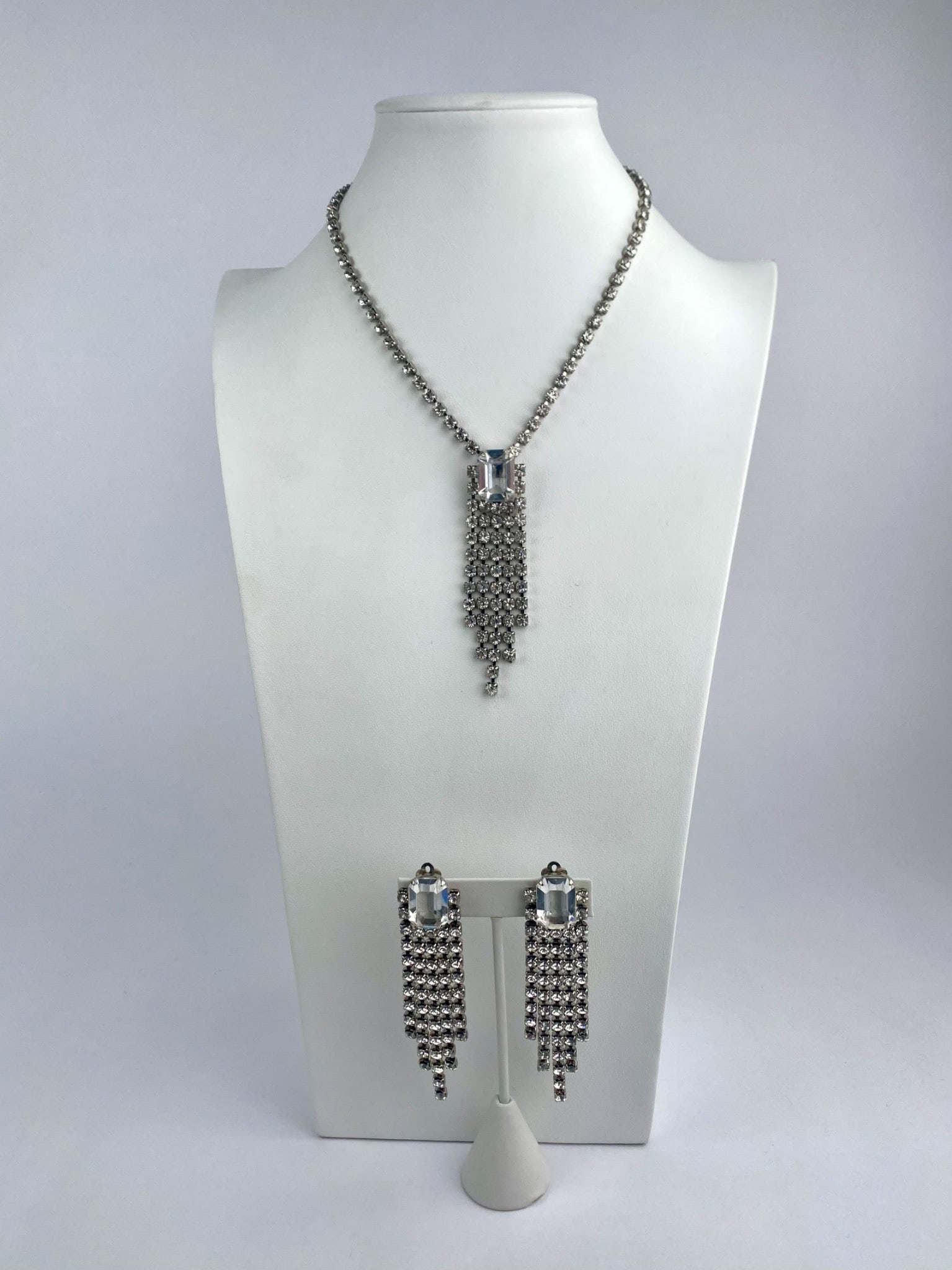 Vintage silver-tone rhinestone jewelry set consisting of a necklace and matching clip-on earrings.: Vintage silver-tone rhinestone jewelry set consisting of a necklace and matching clip-on earrings. The necklace features a sing strand of clear rhinestones suspending a vertical fringe pendant centere