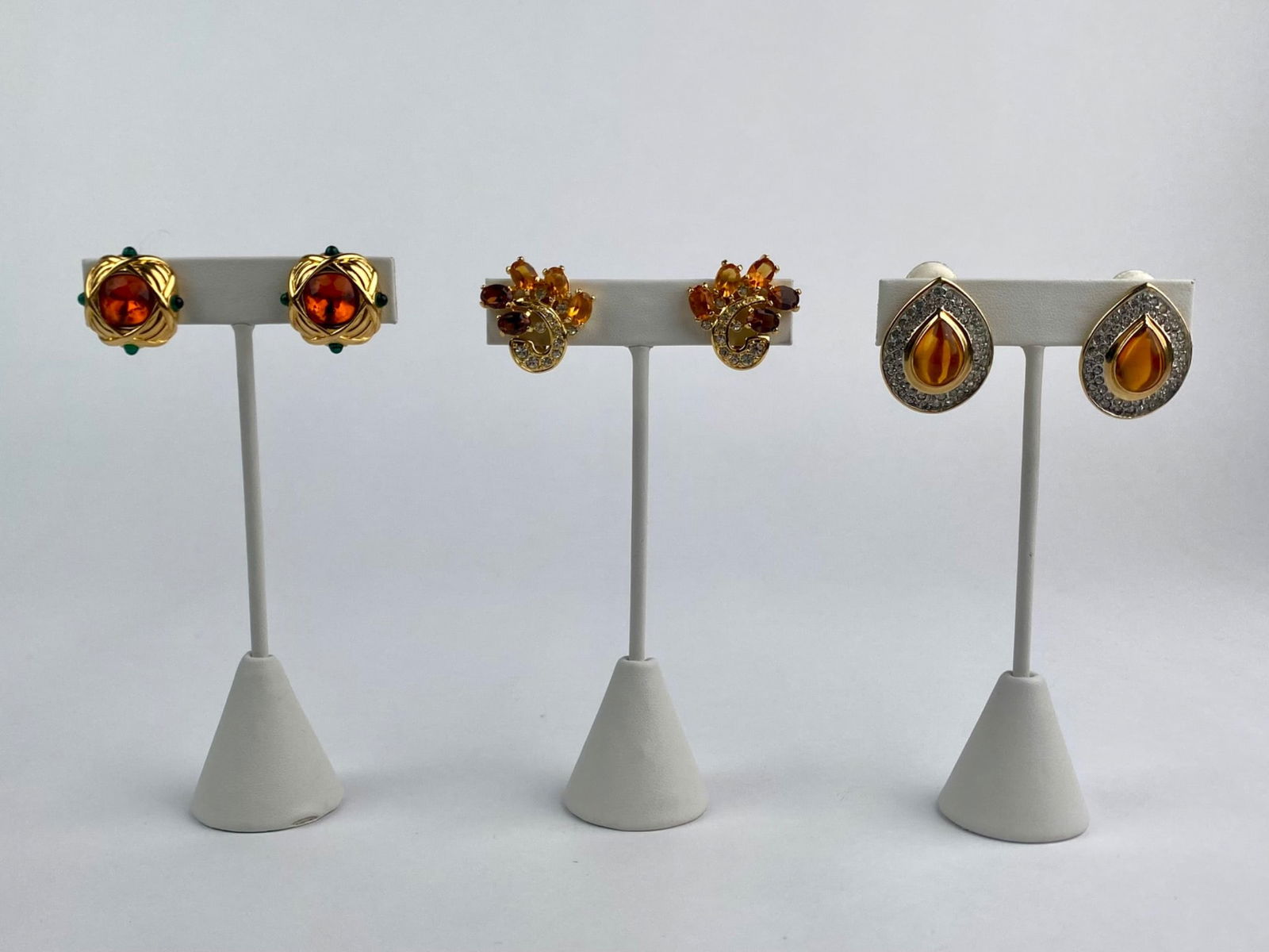 Lot includes three pairs of vintage gold-tone clip-on earrings featuring amber-tone glass cabochons: Lot includes three pairs of vintage gold-tone clip-on earrings featuring amber-tone glass cabochons and rhinestone accents. Two pairs are signed "Nolan Miller," including a floral spray design with fa