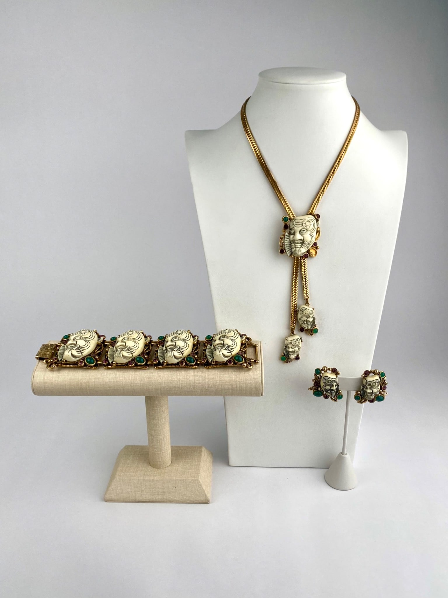 Selro Corp Gold-Tone Mask Motif Necklace, Bracelet & Earrings Set: Vintage costume jewelry set by Selro Corp features carved mask motifs in ivory-tone resin, each accented with green and purple cabochon stones in ornate gold-tone settings. The set includes a statemen