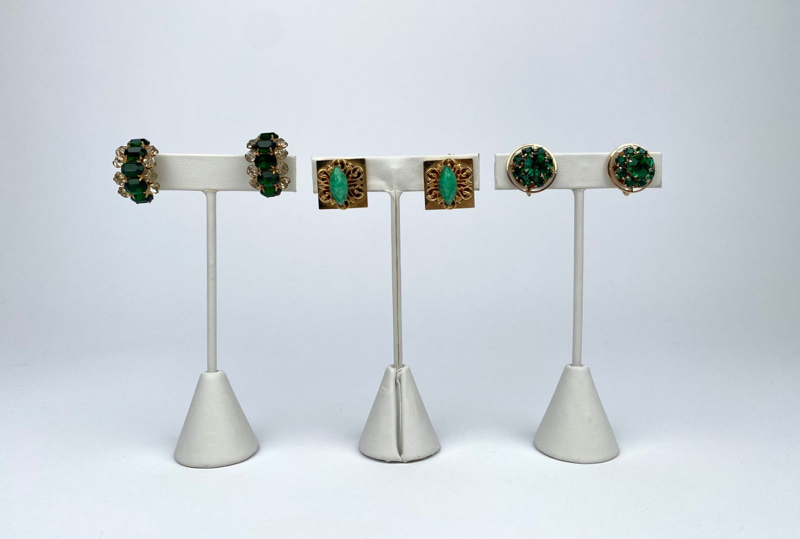 Three Pairs of Gold-Tone & Green Rhinestone Clip Earrings: Three pairs of vintage gold-tone earrings, each featuring green rhinestone embellishments. Includes one pair of screw-back circular earrings with green stones arranged in a floral design, one pair of