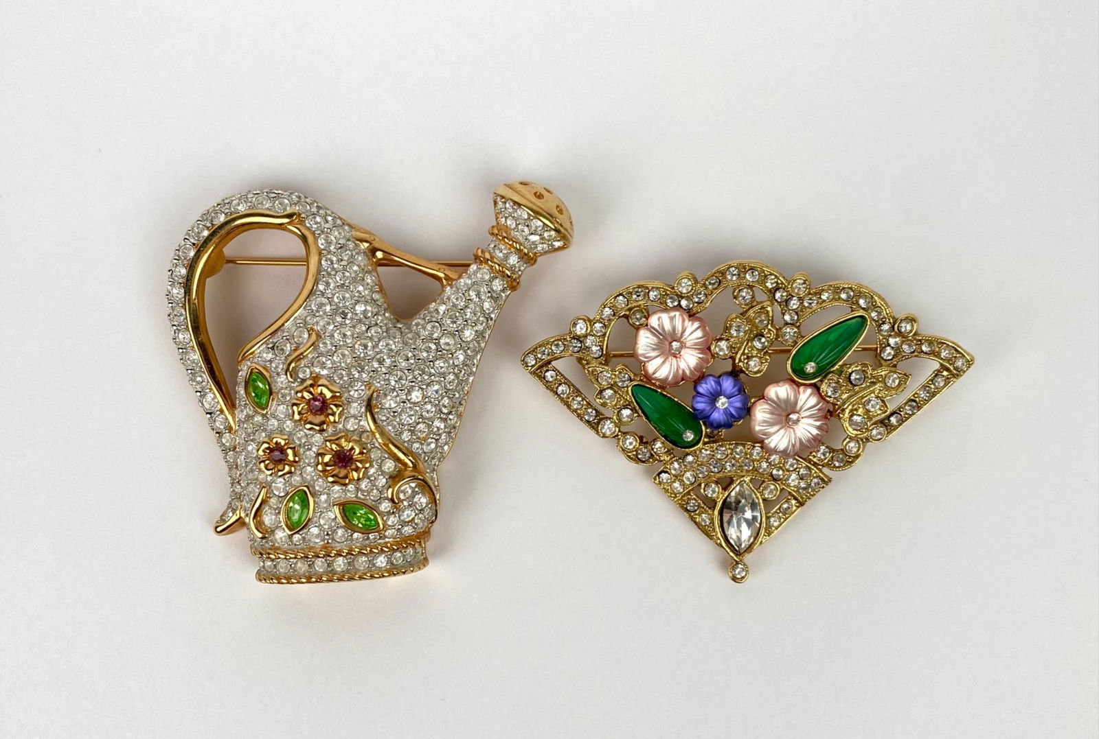 Pair of Brooches Including Swarovski Watering Can & Floral Fan: Gold-tone brooches featuring rhinestone embellishments. Includes a Swarovski watering can-shaped brooch adorned with clear rhinestones, green enamel leaves, and pink floral accents, and a fan-shaped b