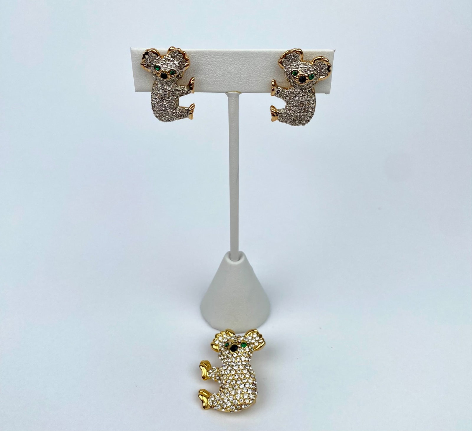 Lewis Segal Koala Clip-On Earrings & Brooch With Rhinestone Accents: A pair of koala-shaped clip-on earrings and a matching brooch, each featuring rhinestone accents and green stone eyes by Lewis Segal. The earrings are designed with gold-tone metal backs, and the broo