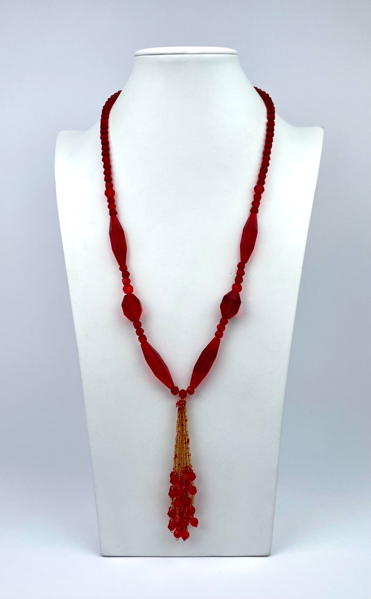Red glass bead necklace featuring a variety of bead shapes, including faceted and elongated designs.: Red glass bead necklace featuring a variety of bead shapes, including faceted and elongated designs. The necklace is designed with a decorative tassel, composed of gold-tone beads interspersed with sm