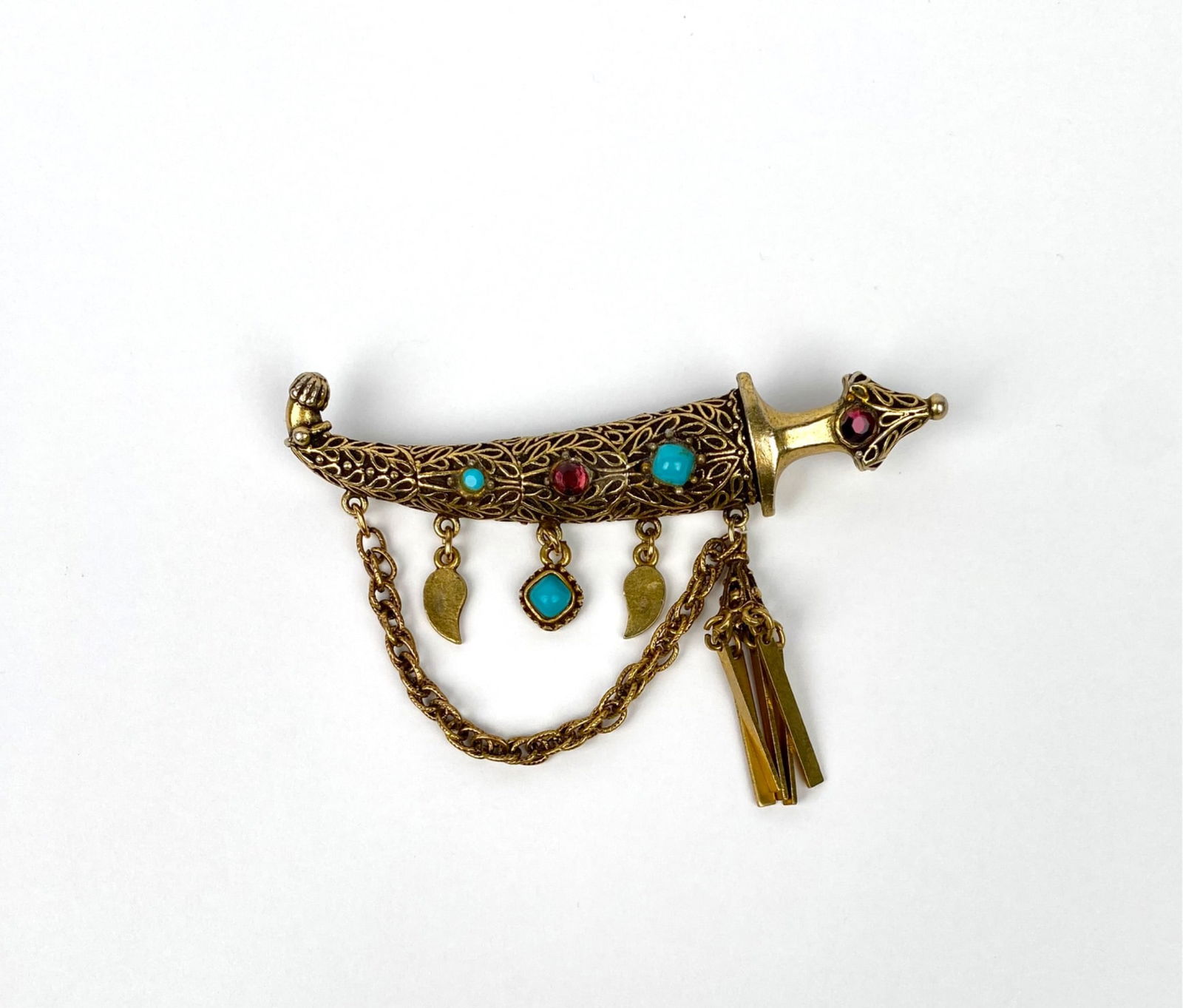 Vintage Hollycraft Gold-Tone Jeweled Dagger Brooch with Dangling Charms: A Hollycraft gold-tone metal brooch shaped like a dagger, adorned with turquoise and ruby-colored stones. Features intricate filigree work and assorted dangling charms, including tasseled chains and s