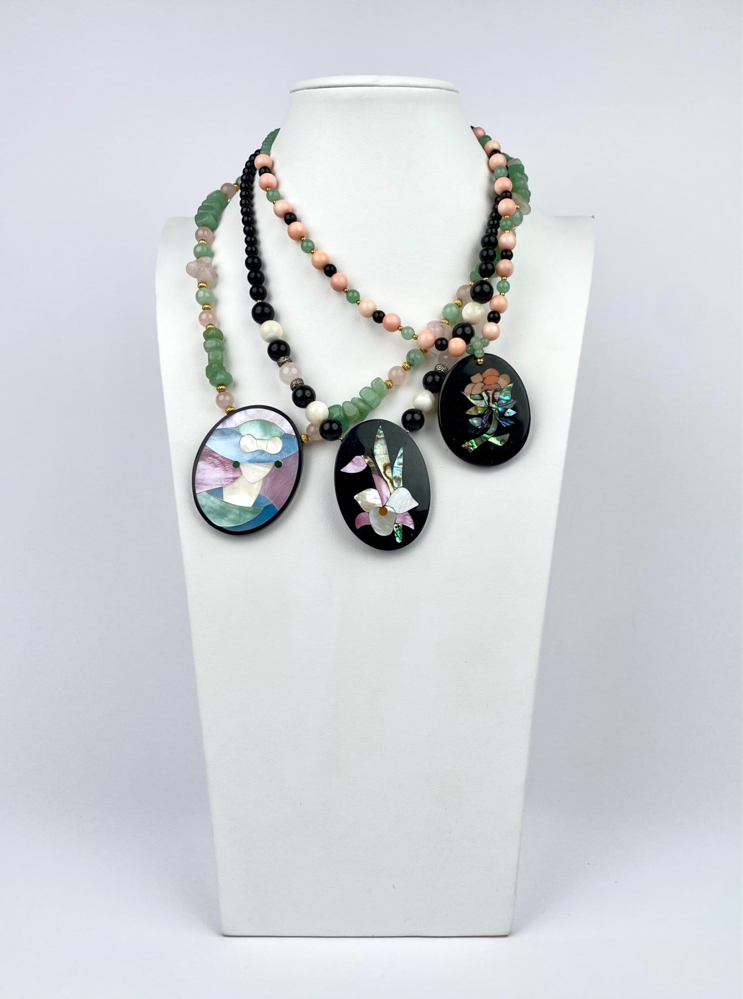 Three necklaces by Lee Sands. Each necklace features beaded strands with a central inlaid pendant: Three necklaces by Lee Sands. Each necklace features beaded strands with a central inlaid pendant showcasing intricate designs made of natural materials. Beads include green, black, pink, and cream-co