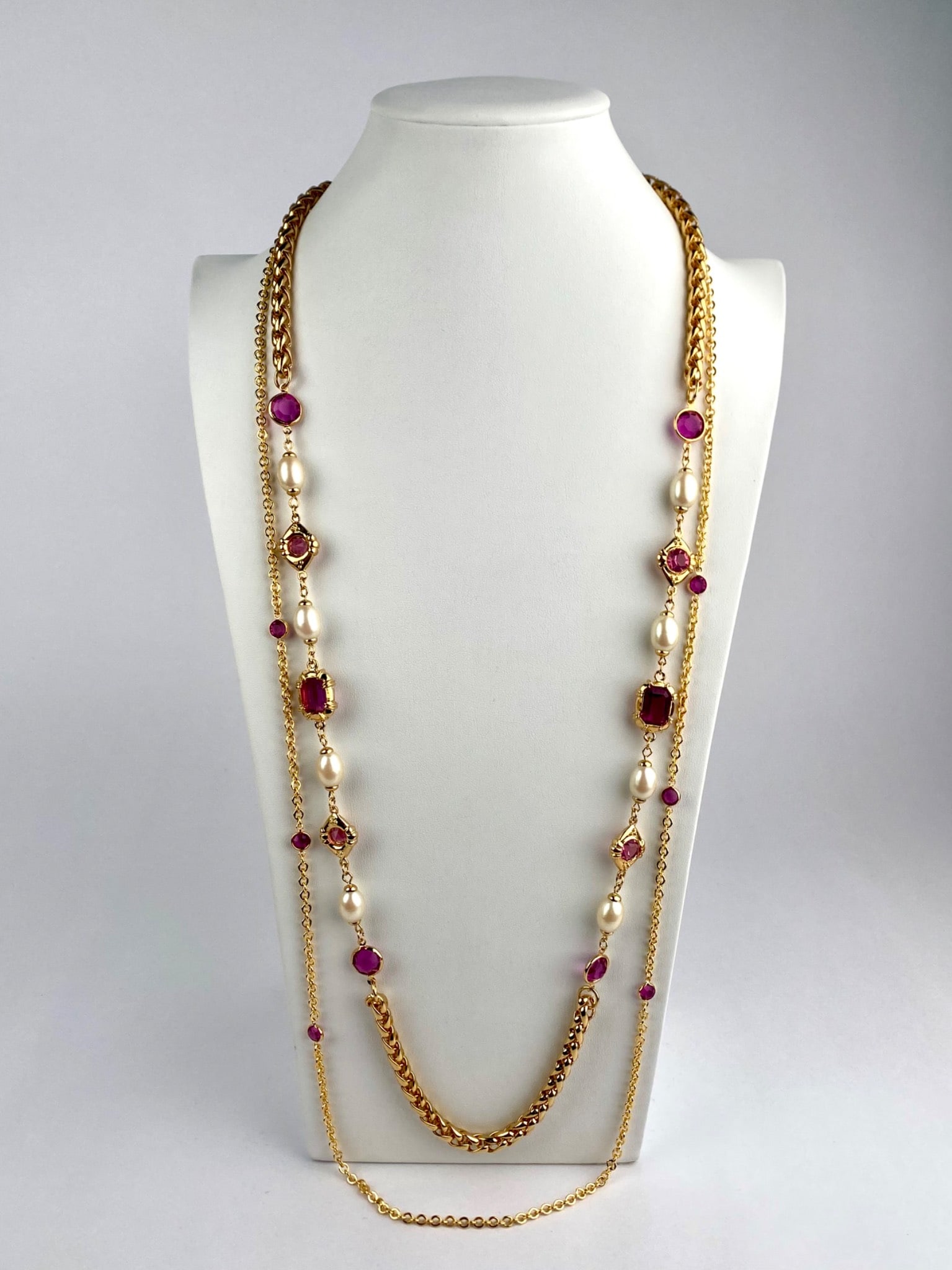 Pair of Gold-Tone Station Necklaces with Pink Crystal Accents: Lot includes two gold-tone station necklaces. The first necklace features alternating faux pearls and faceted pink crystal stations set along a woven gold-tone chain. The second necklace is a delicate