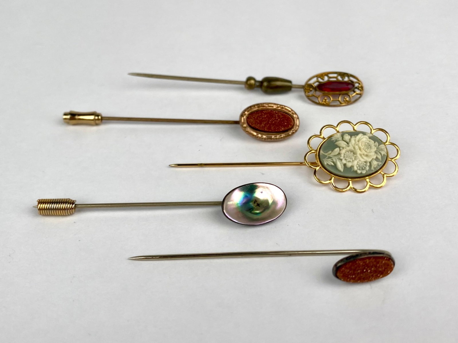 Vintage group includes five decorative stick pins featuring varied designs and materials. The: Vintage group includes five decorative stick pins featuring varied designs and materials. The assortment includes oval goldstone-style cabochons in gold-tone frames, an iridescent shell example, a pie