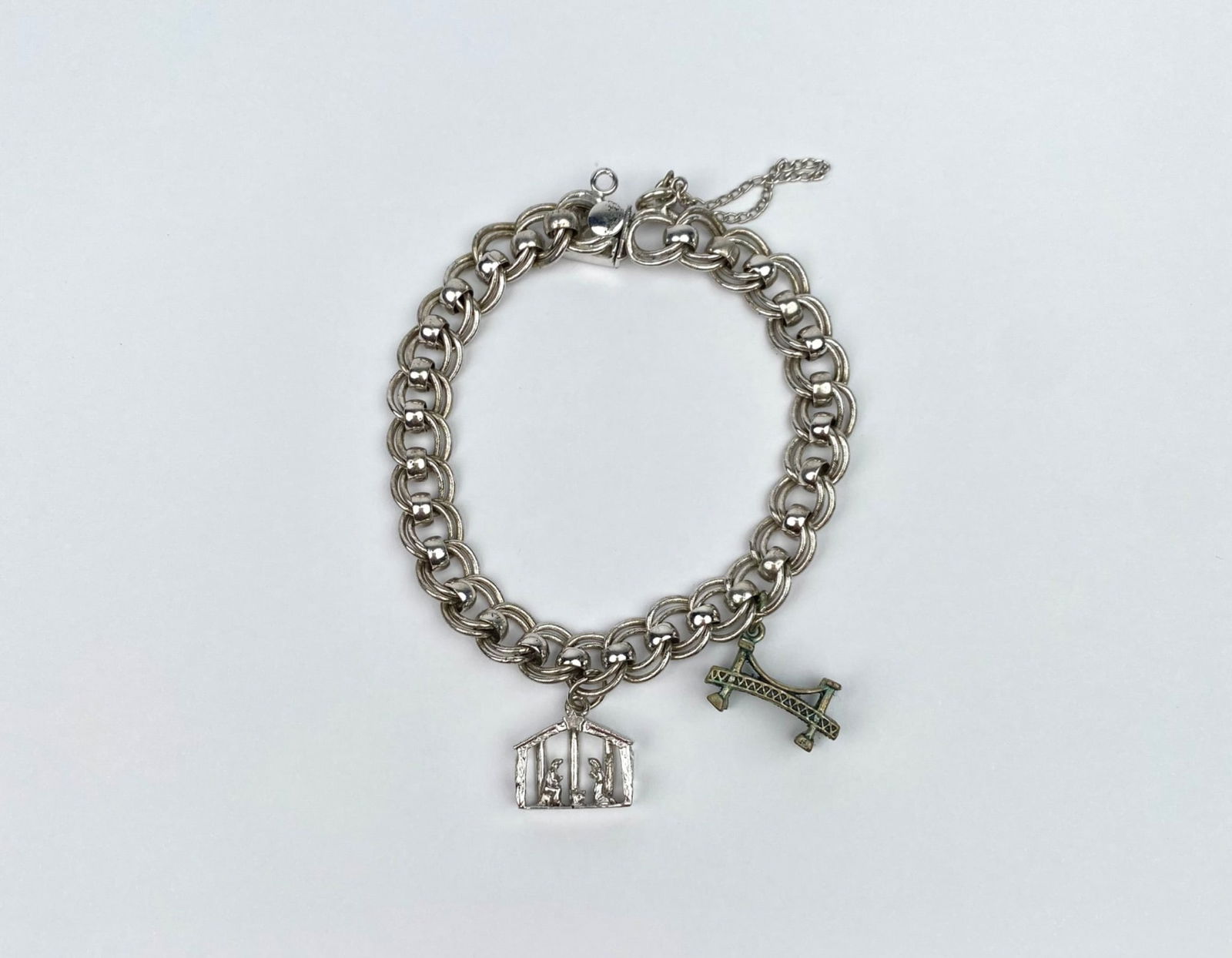 Jacoby-Bender Sterling Silver Charm Bracelet with Charms: Jacoby-Bender sterling silver charm bracelet featuring a bold link design. Includes two charms: a nativity scene and a bridge design with green enamel accents. Marked ‘JB Sterling’ on the clasp. F