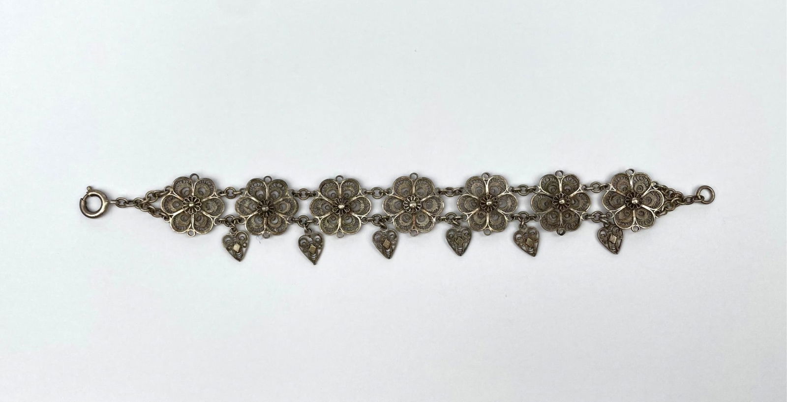 Vintage Silver-Tone Filigree Floral Bracelet with Heart Pendants: A delicately crafted silver-tone filigree bracelet featuring floral motifs adorned with intricate details and accented by dangling heart-shaped pendants. The bracelet includes a secure spring ring cla