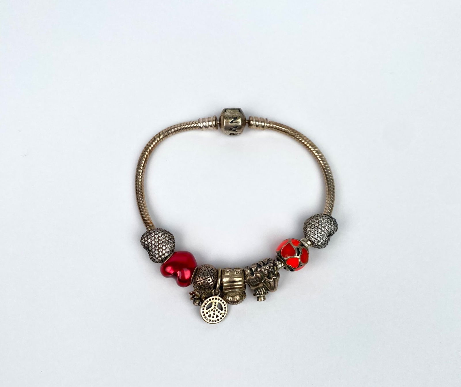 Pandora Sterling Silver Bracelet with Charms Featuring Red & Silver Tones: Pandora bracelet crafted from sterling silver and adorned with various charms in red and silver tones. Features include a mixture of decorative elements such as hearts, a tree motif, and ornate bead d