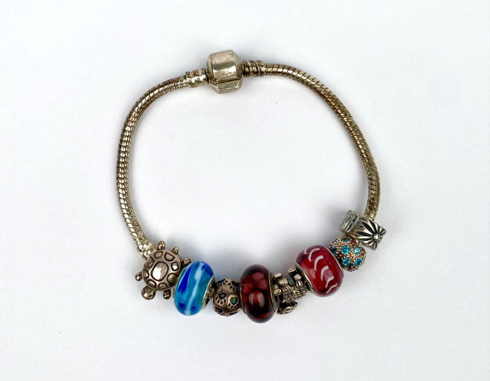 Silver-Tone Charm Bracelet with Mixed Glass & Silver Charms: Silver-tone bracelet with a snake chain design, featuring a variety of glass and metal beads. The bracelet includes beads with designs such as a turtle motif, red and blue glass accents, textured meta