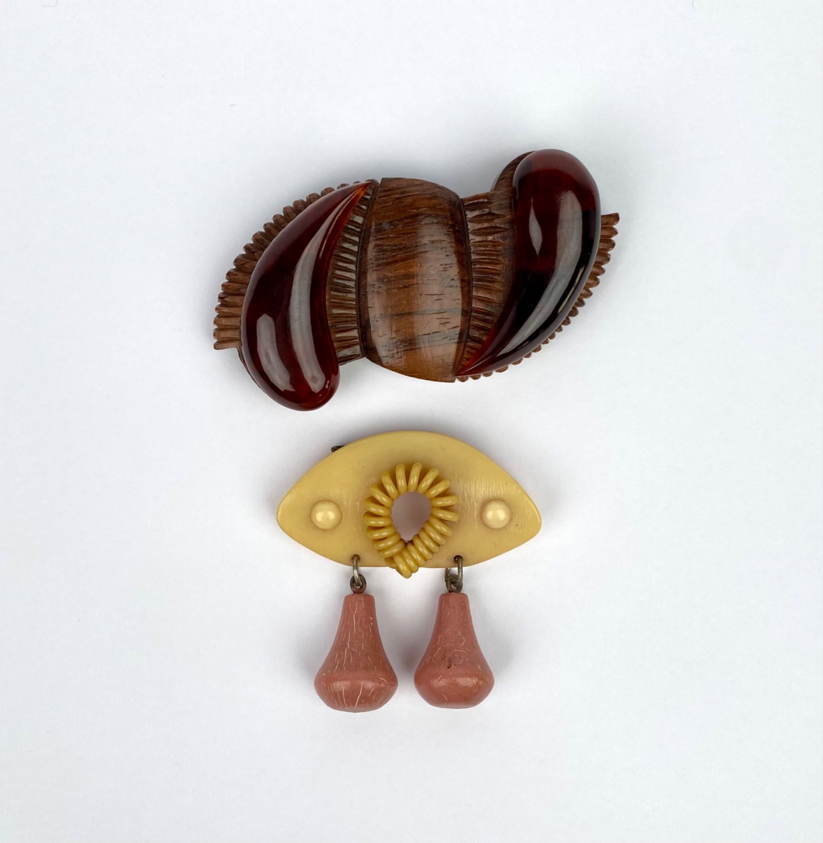 Two Mid-Century Mixed Material Brooches: Two brooches, one crafted from resin and wood in a sculptural layered design featuring red and brown tones underpins, and the other composed of plastic in a light yellow and pink color scheme with dro