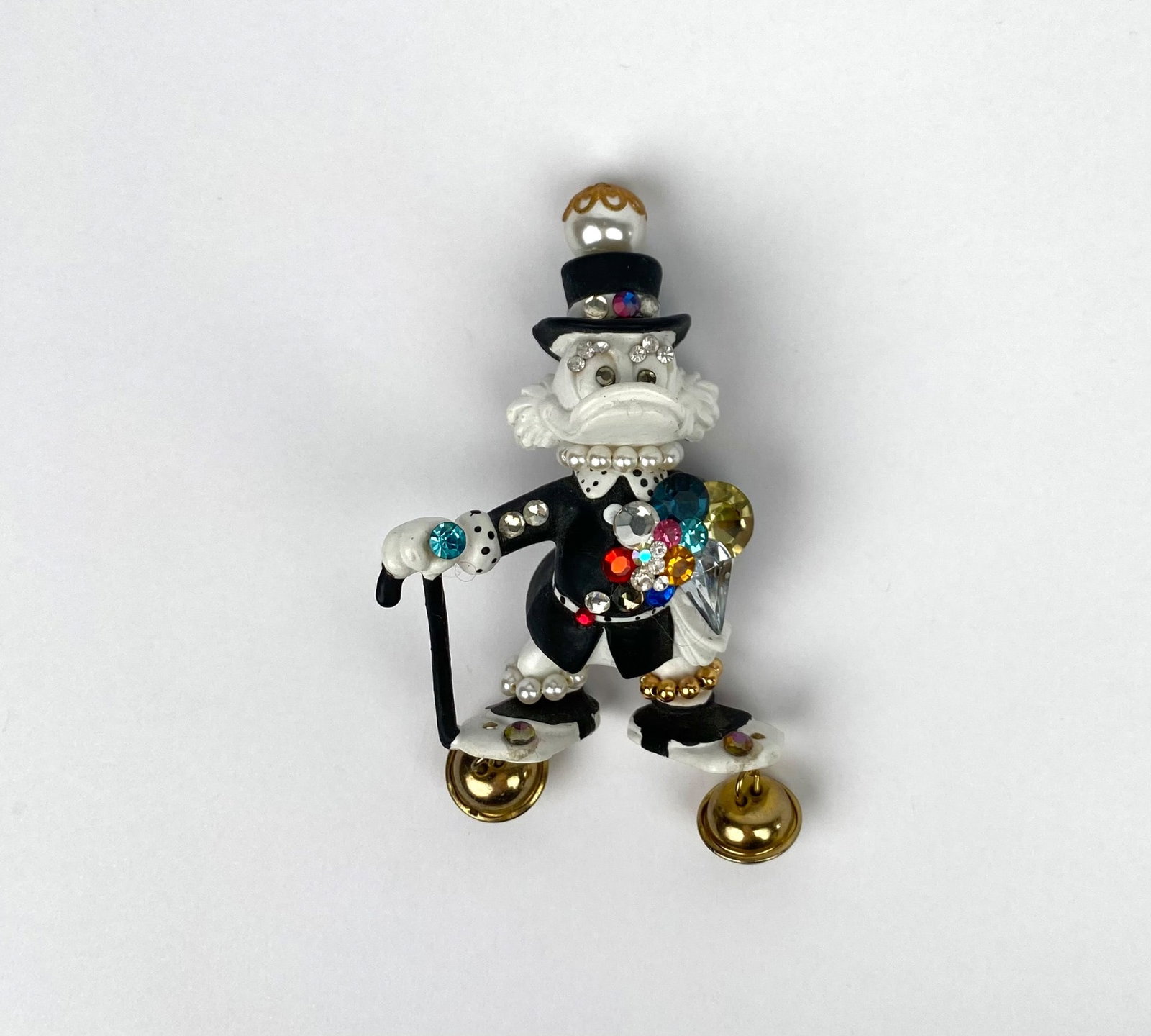 Vintage figural brooch depicting Scrooge McDuck, produced by Walt Disney Productions. The brooch is: Vintage figural brooch depicting Scrooge McDuck, produced by Walt Disney Productions. The brooch is enameled in white and black, adorned with faux rhinestones, beads, and gold-tone accents. Additional