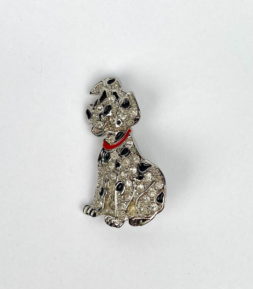 Silver-tone Disney brooch in the shape of a Dalmatian, with black enamel spots and clear crystal: Silver-tone Disney brooch in the shape of a Dalmatian, with black enamel spots and clear crystal accents. Features a glossy red enamel collar and a secure pin-back closure. Marked on the reverse with