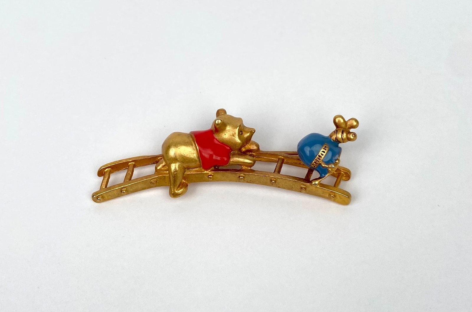 Vintage Disney Winnie the Pooh & ‘HUNNY’ Jar Bridge Brooch: Vintage Winne the Pooh brooch featuring Pooh and a 'HUNNY' jar. The brooch includes a secure pin clasp on the back. | Please see photos for additional details. | Dimensions: .5 x 2.25 in | Weight: