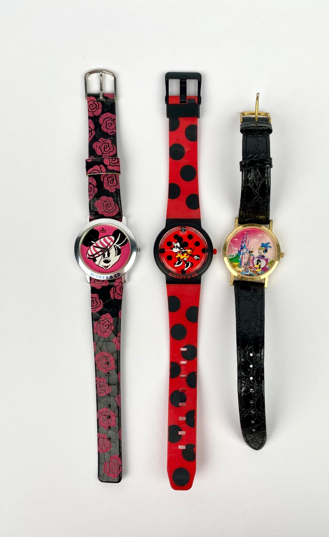 Three Disney Minnie Mouse watches. The first watch features a pink and black design with Minnie: Three Disney Minnie Mouse watches. The first watch features a pink and black design with Minnie Mouse in a striped hat. The second watch showcases a red and black polka dot design with Minnie Mouse on