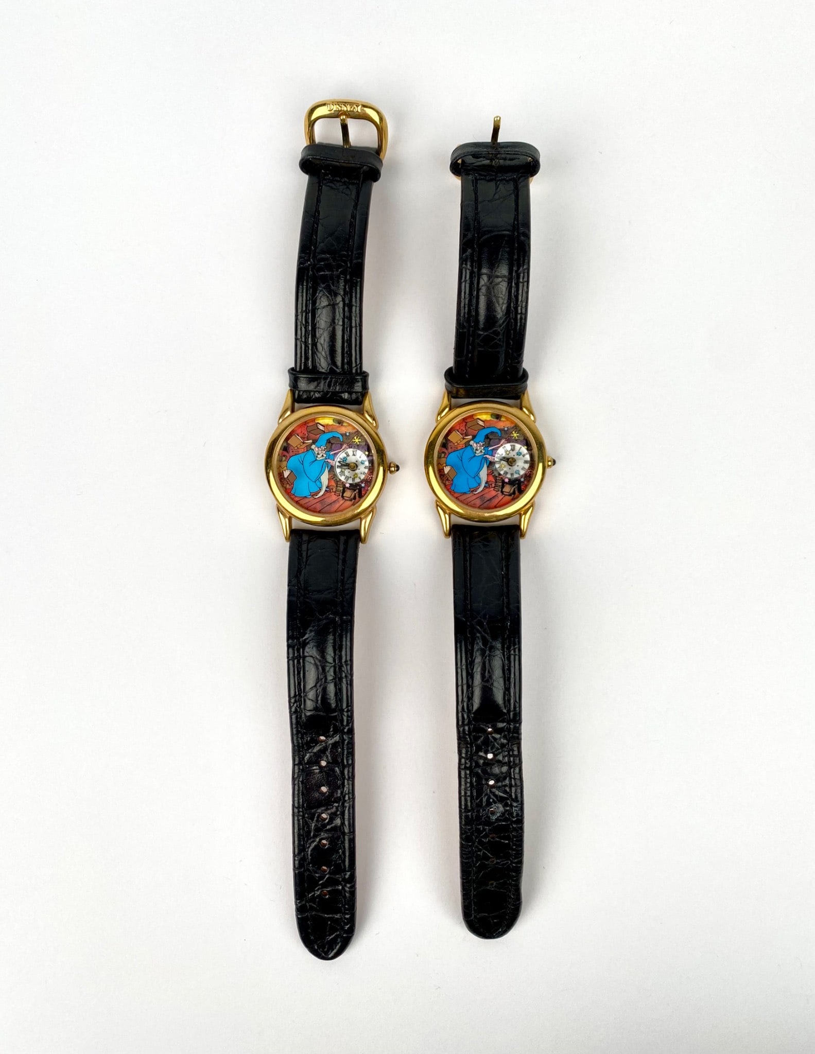 This is a pair of Disney Watch Collectors Club Fossil watches in 'The Sword in the Stone' Series: This is a pair of Disney Watch Collectors Club Fossil watches in 'The Sword in the Stone' Series III. Each watch features a themed dial, black leather strap, and gold-tone buckle. Case backs identify
