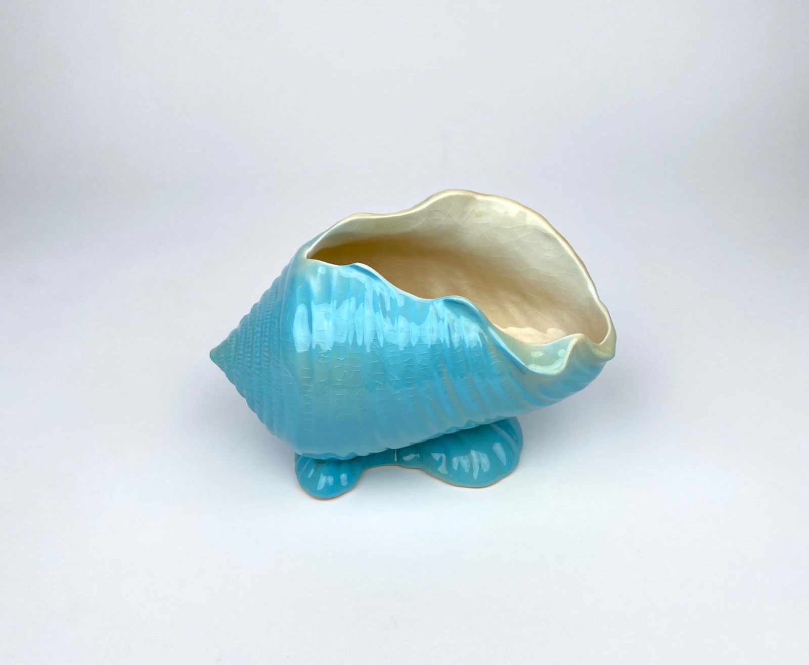 Blue ceramic shell-shaped vase or planter by Roseville Pottery, USA. Features a glossy glaze with: Blue ceramic shell-shaped vase or planter by Roseville Pottery, USA. Features a glossy glaze with detailed ribbed shell pattern and cream interior. Maker’s mark, ‘563 Roseville U.S.A.’ embossed