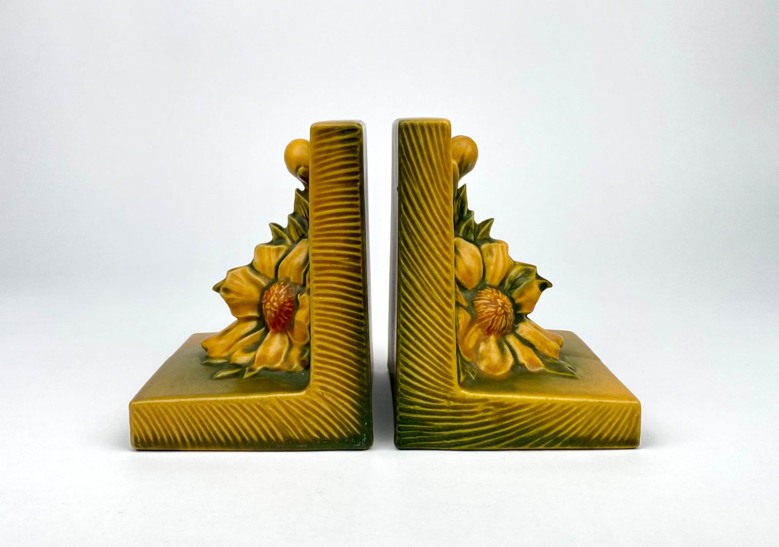 Ceramic bookends by Roseville Pottery in the peony pattern, featuring a yellow and green glaze with: Ceramic bookends by Roseville Pottery in the peony pattern, featuring a yellow and green glaze with a raised peony motif. Both pieces are marked “Roseville, U.S.A. 11” on the bases. Both booke
