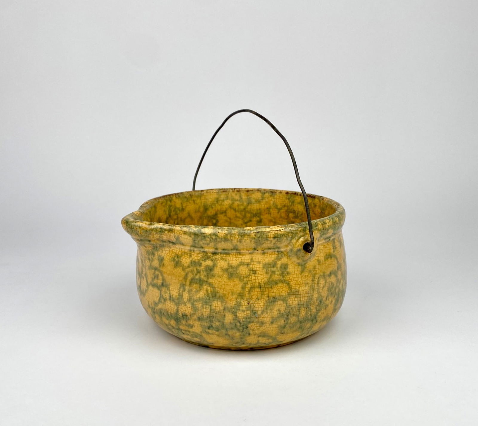 Early Roseville Sponge Ware Batter Bowl: Yellow and green glazed ceramic batter bowl featuring a sponge ware pattern and a distinctive wire handle for carrying or hanging. The piece shows visible surface crazing and wear indicative of age an