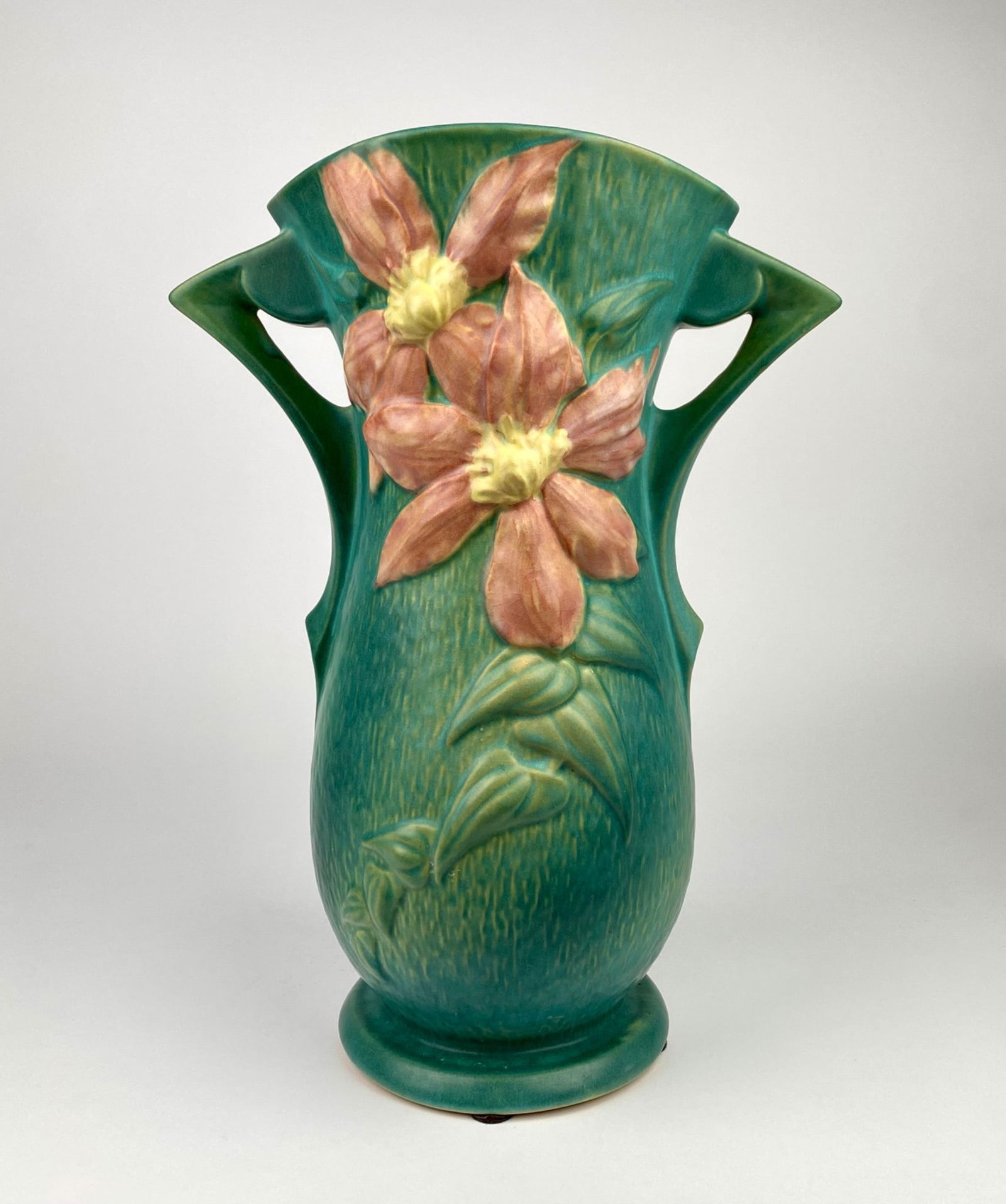 Large Roseville Pottery Clematis Vase, Model 114, USA: Roseville Pottery vase featuring the Clematis pattern, showcasing pink and yellow flowers with raised detailing on a green ground. The design includes two angular handles and stylized floral motifs. M